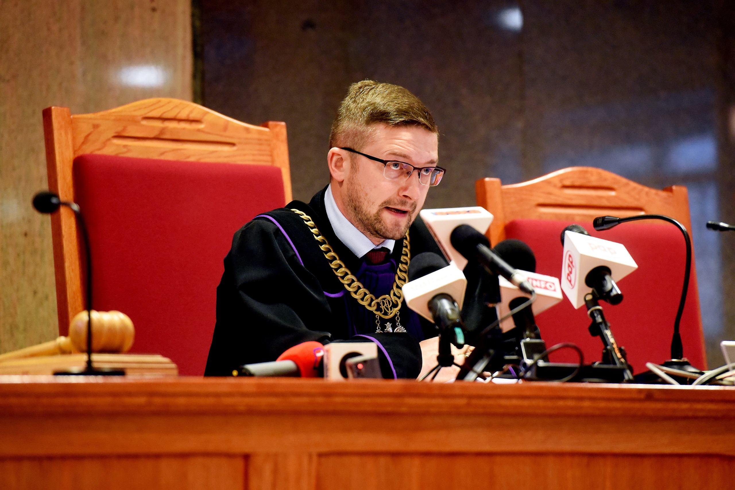 Sędzia Juszczyszyn siedzi za stołem sędziowskim w todze i w łańcuchu