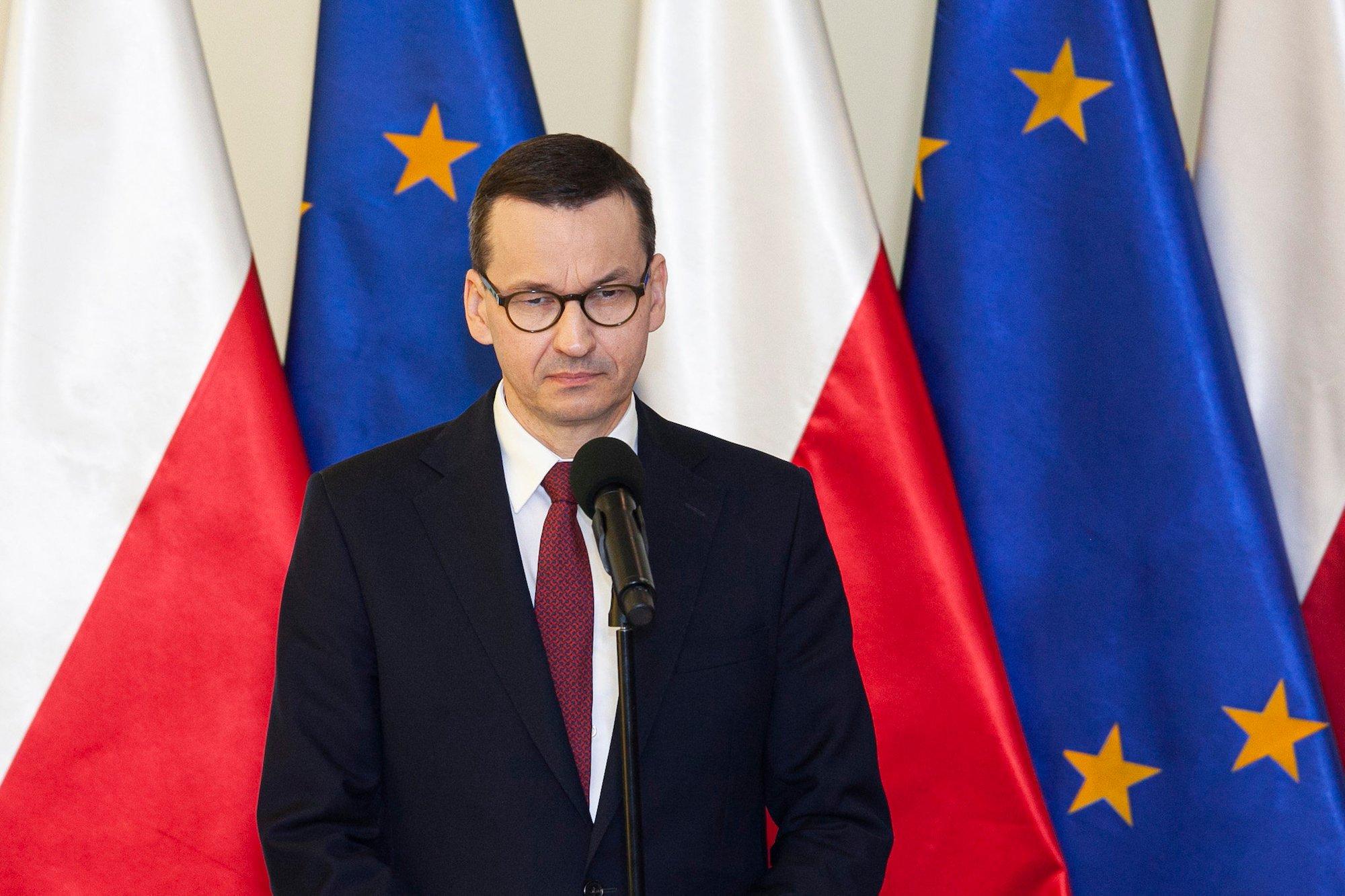 Mateusz Morawiecki na tle flag Polski i UE