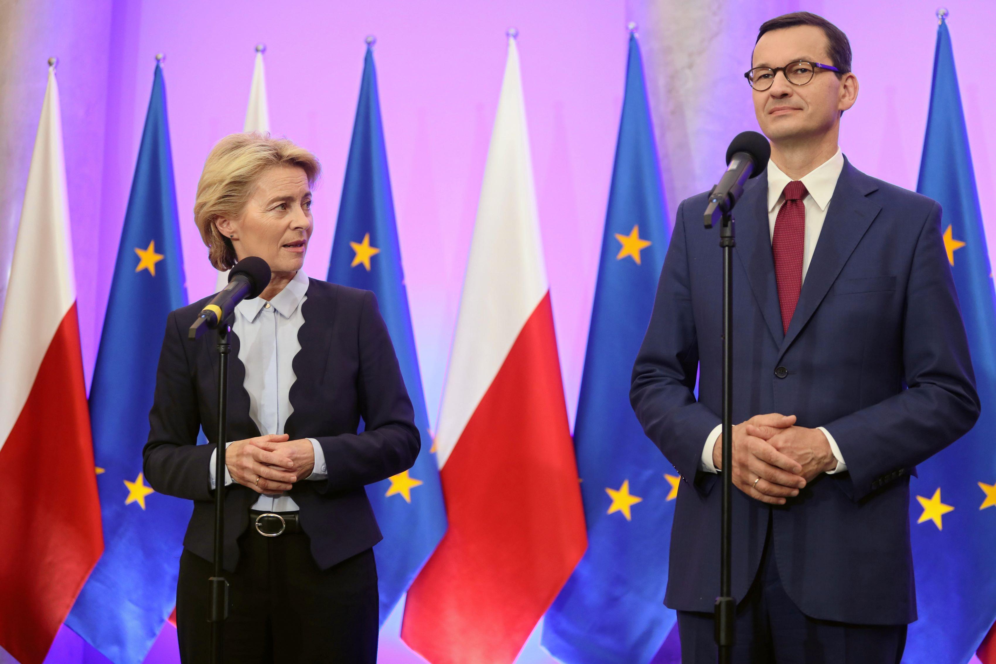 Mateusz Morawiecki i Ursula von der Leyen stoją na tle flag polskich i europejskich.