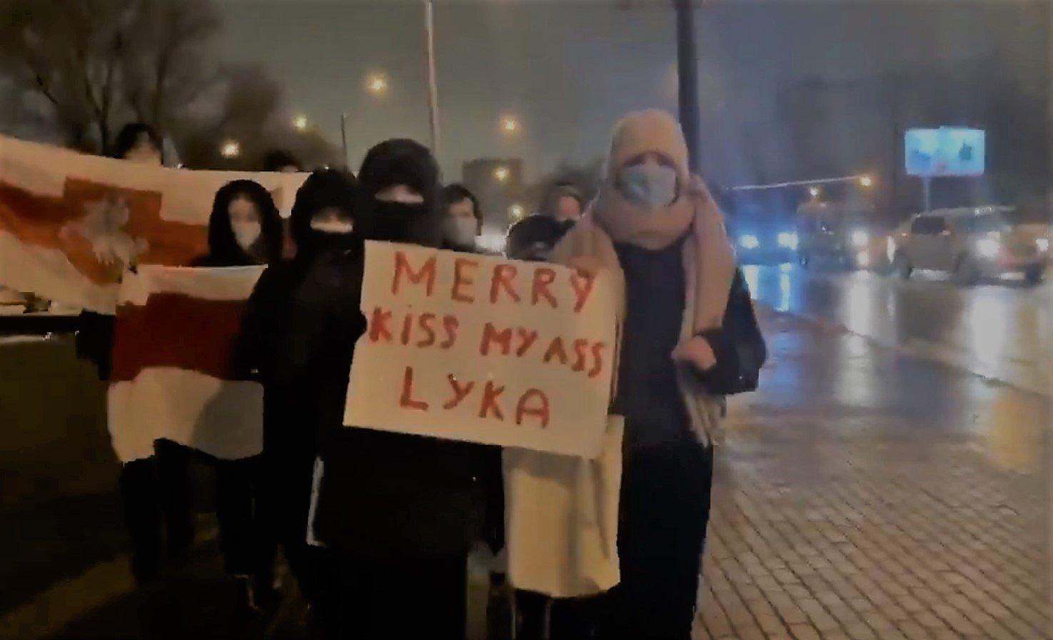 Protest w Mińsku, ludzie w maseczkach niosą plakat z napisem Merry Kiss My Ass Luka