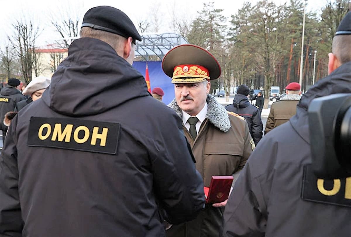 Łukaszenka w wojskowym mundurze i czapce wręcza order funkcjonariuszowi OMON
