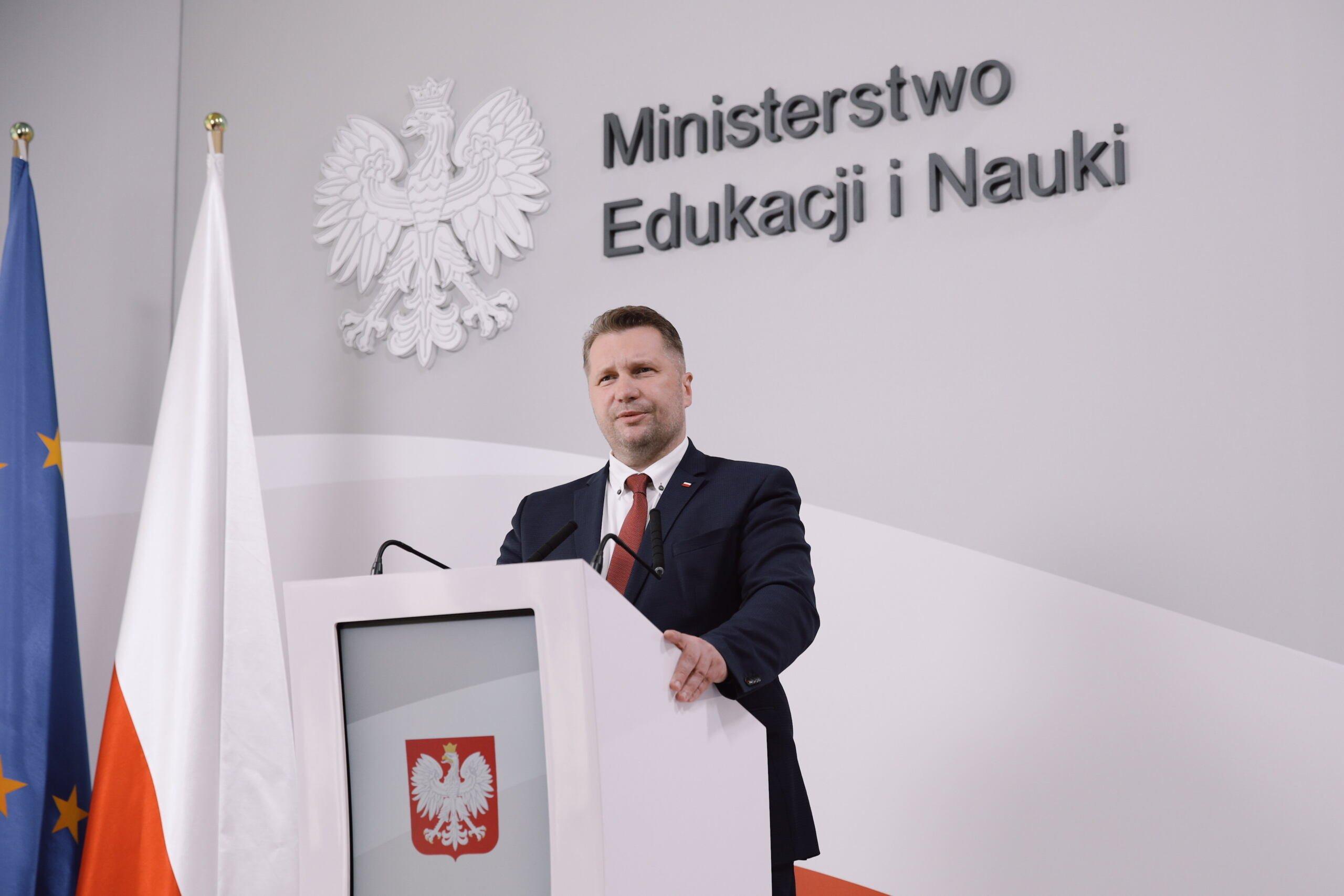 Minister Przemysław Czarnek stai na tle logo ministerstwa edukacji i przemawia