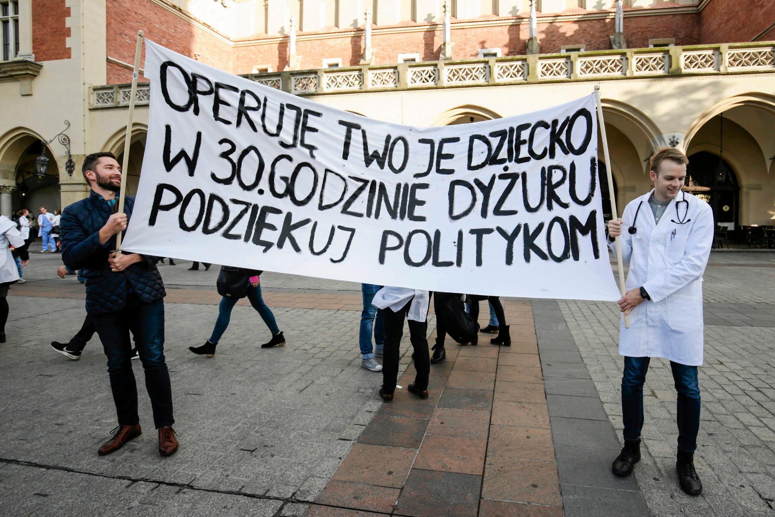 Osoby trzymające transparent z napisem „Operuję twoje dziecko w 30 godzinie dyżuru. Podziękuj politykom" podczas manifestacji solidarnościowej ze strajkującymi rezydentami, Rynek Główny w Krakowie, 2017 rok