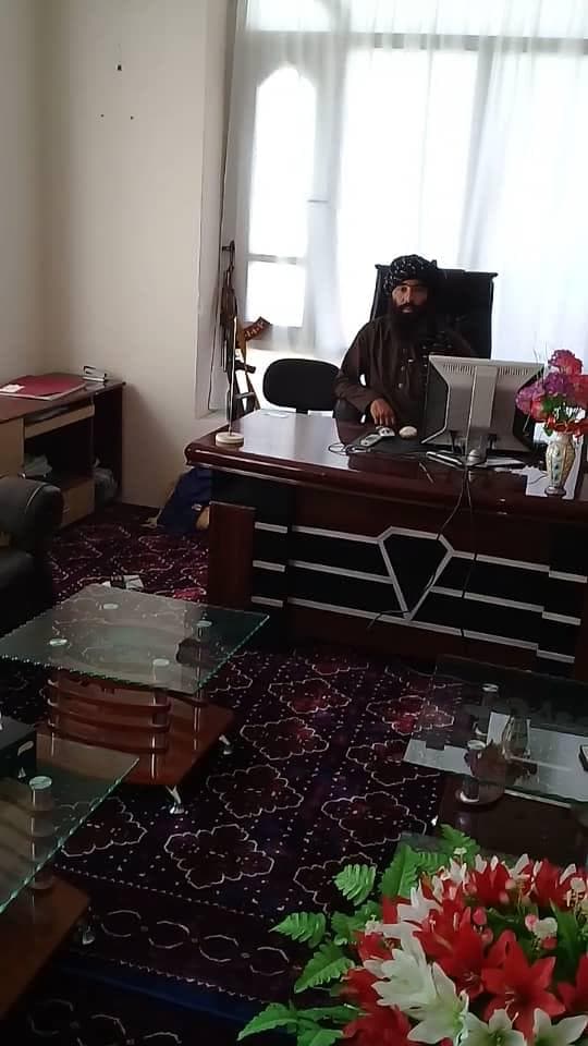 Talib za biurkiem w biurze Fahima, przy ścianie stoi jego karabin