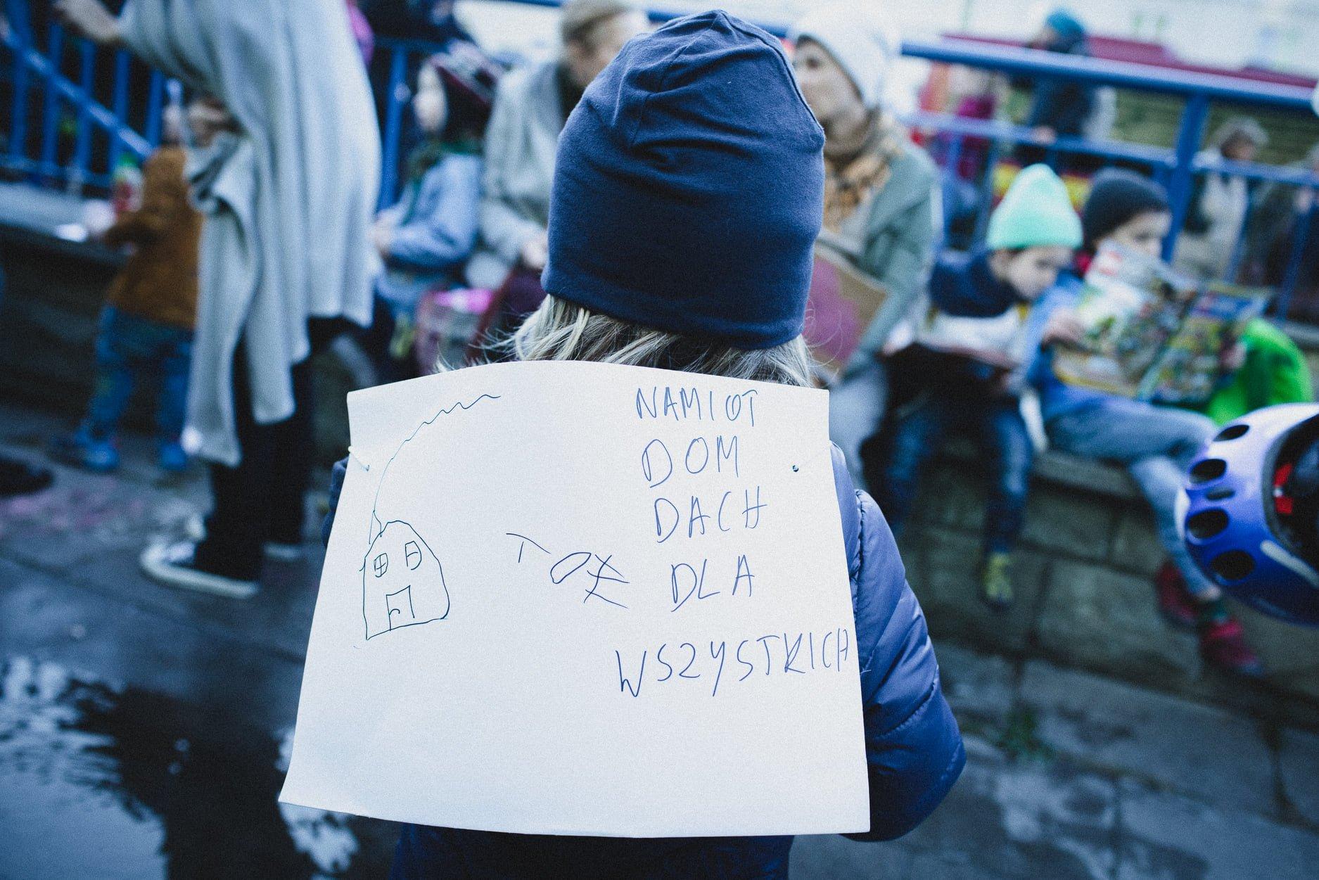 Dziecki z rysunkiem domu dla uchodźców przed siedziba straży granicznej w Warszawie