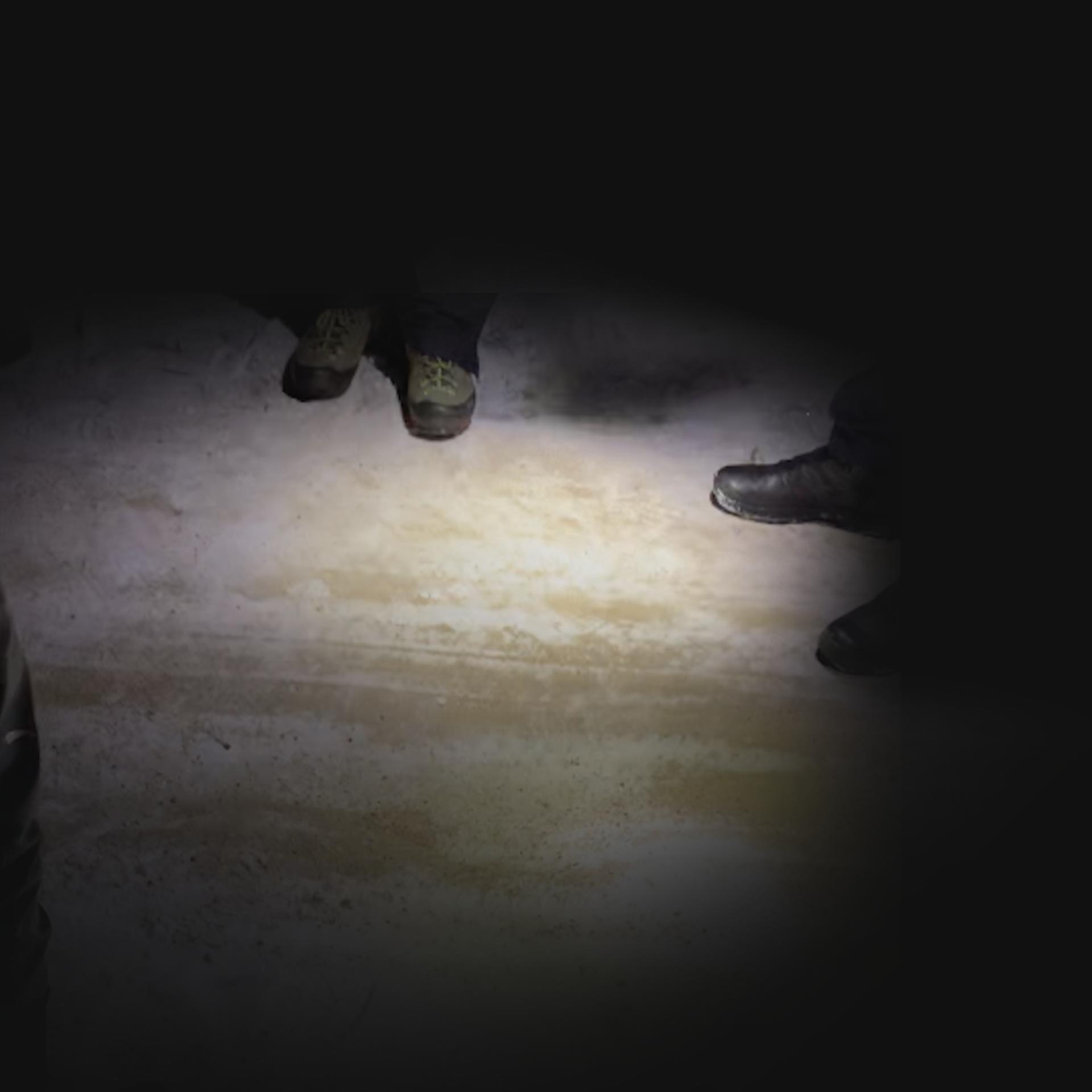 Zdjęcie wykonane w nocy, widoczne są na nim dwie pary butów na piaskowej, oszronionej drodze