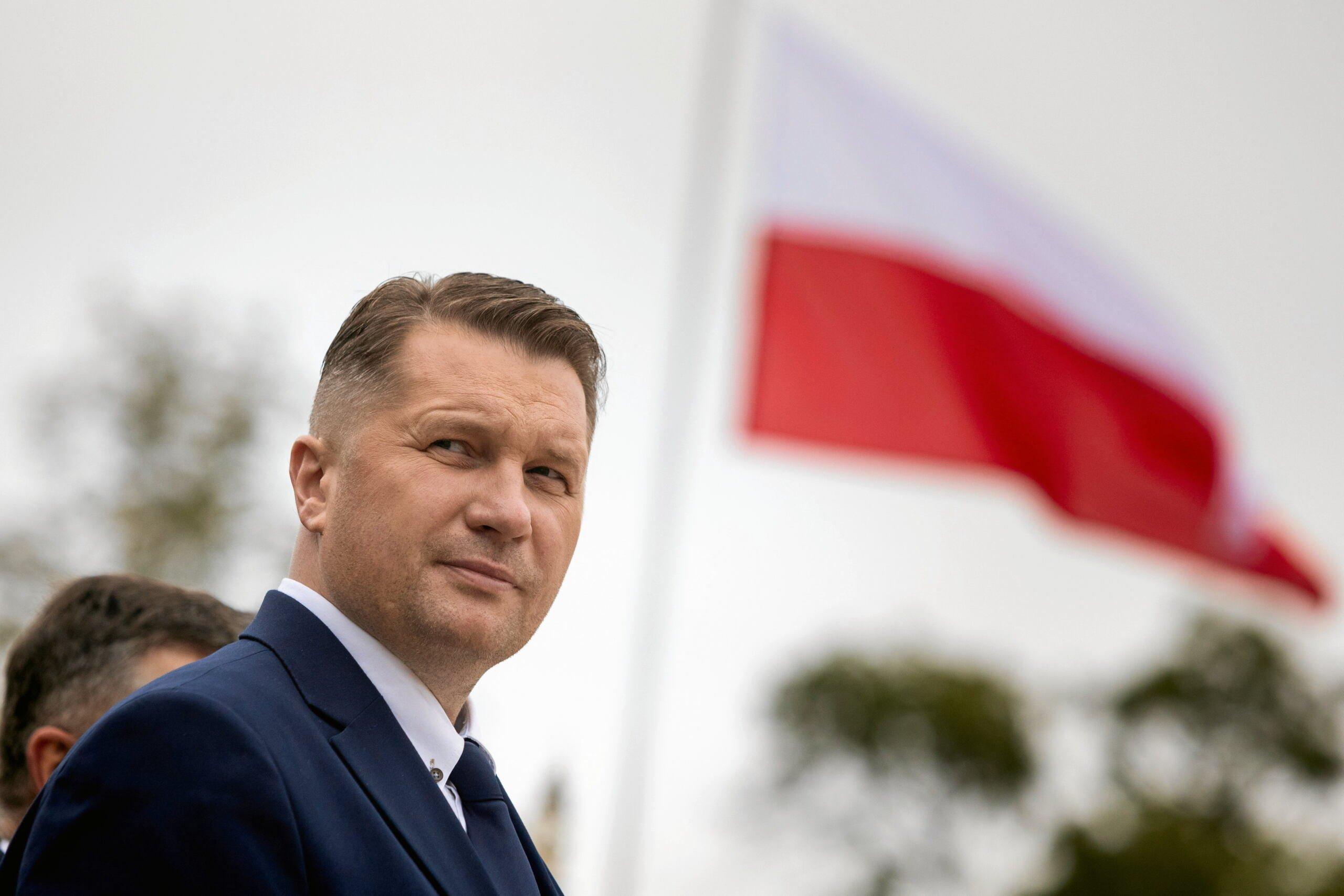 Przemysław Czarnek stoi na tle biało-czerwonej flagi