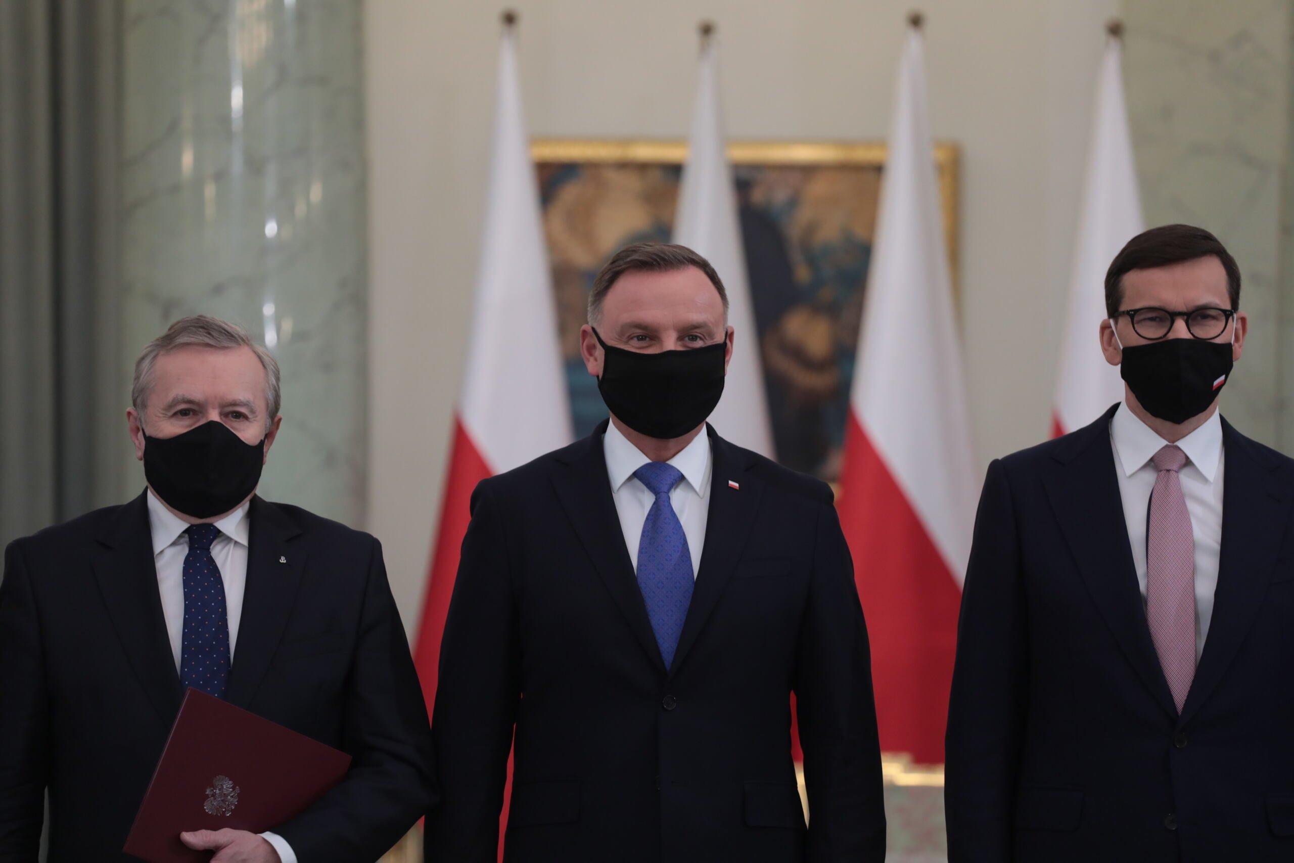 Piotr Gliński, Andrzej Duda i Mateusz Morawiecki na tle biało-czerwonych flag