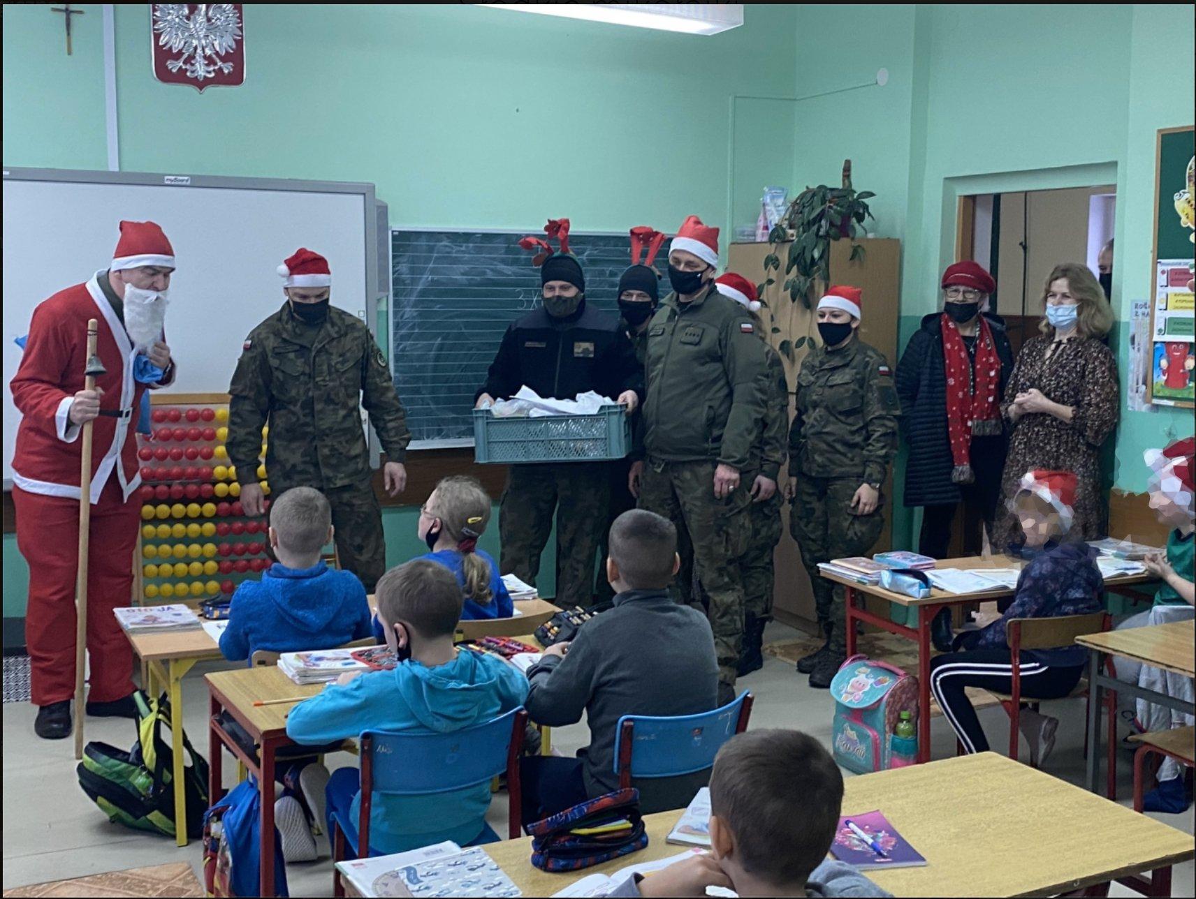 Żołnierze w czapkach mikołajów wnosza prezenty do klasy szkolnej
