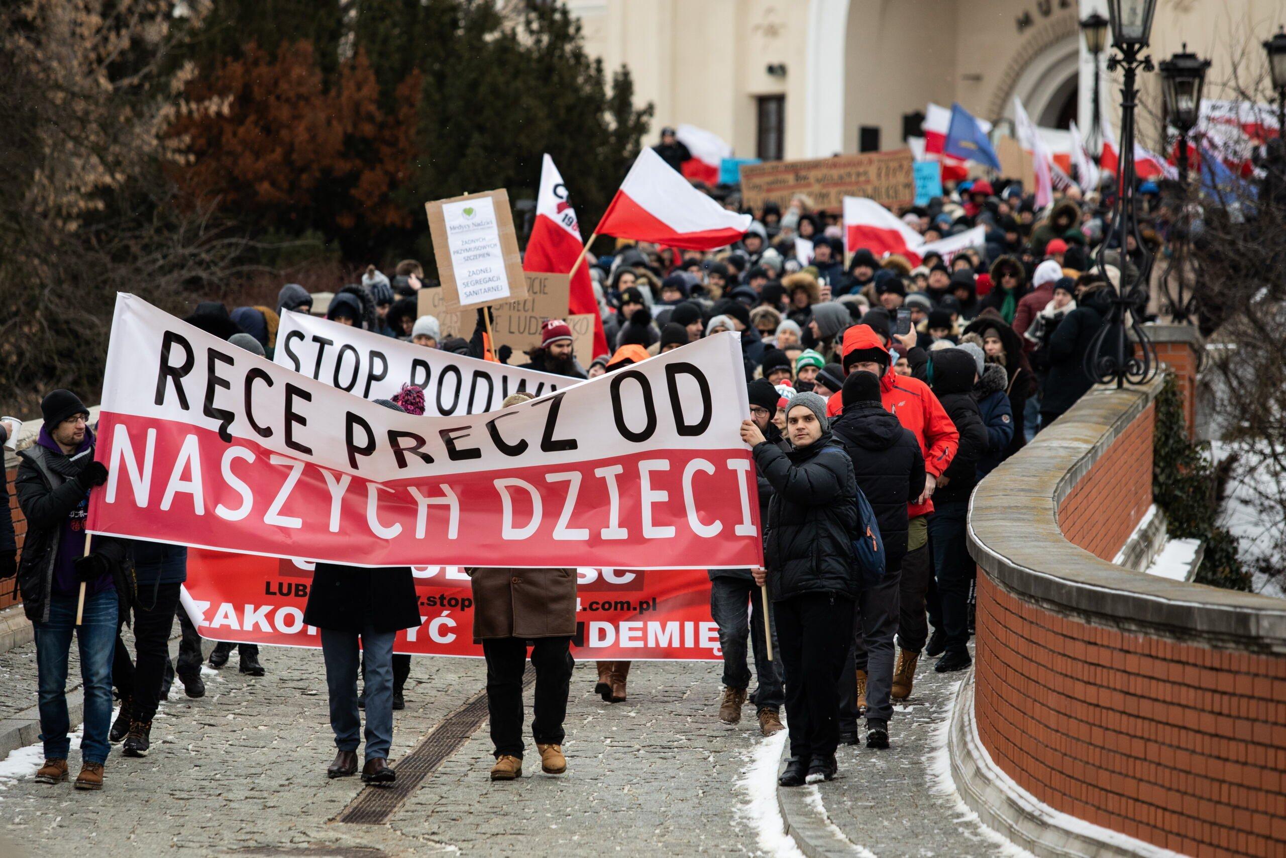 Marsz antyszczepiokowców, idą ulicą w Lublinie z transparentem "Ręce precz od naszych dzieci"