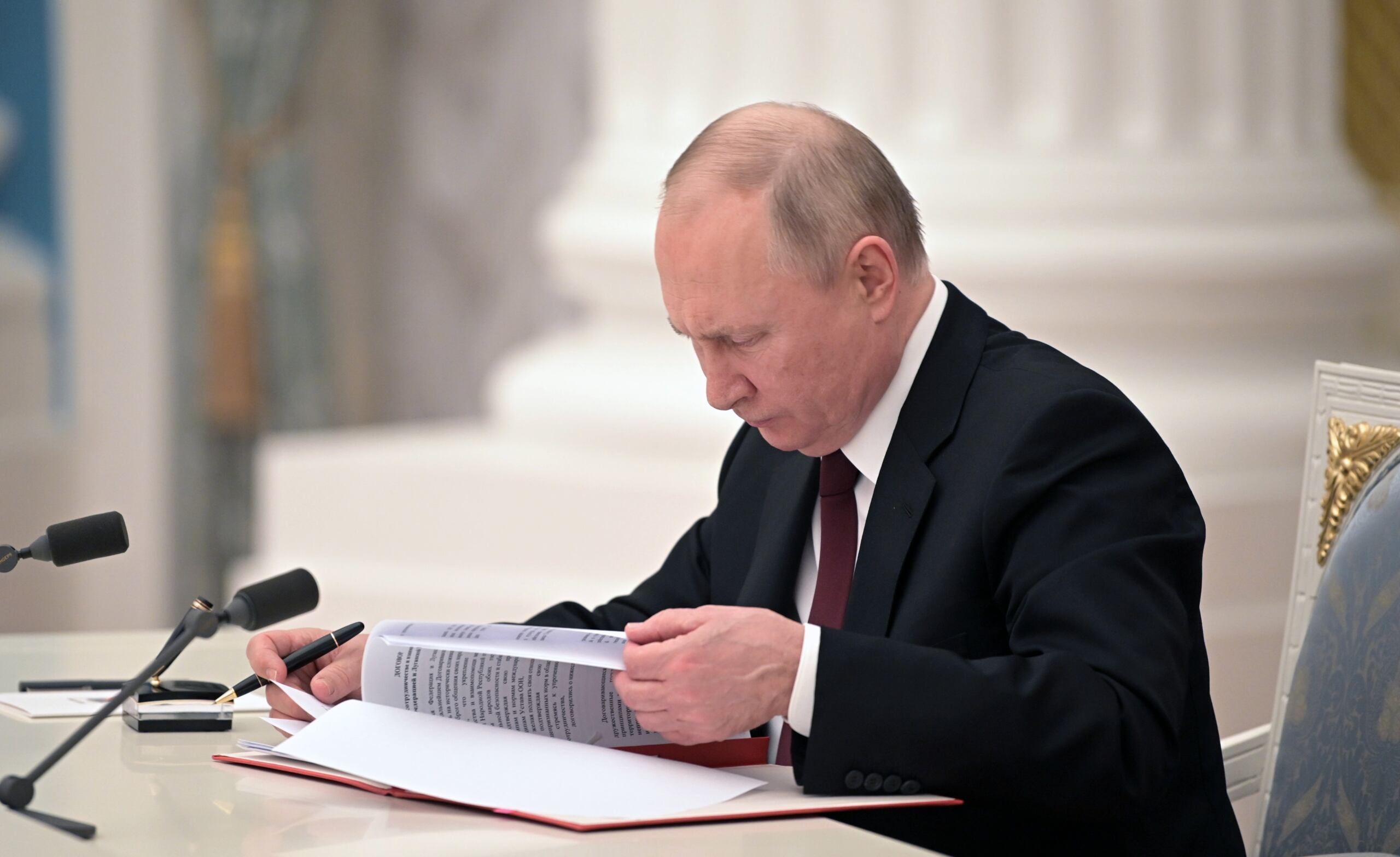 Prezydent Rosji Władimir Putin czyta dokument w sali na Kremlu