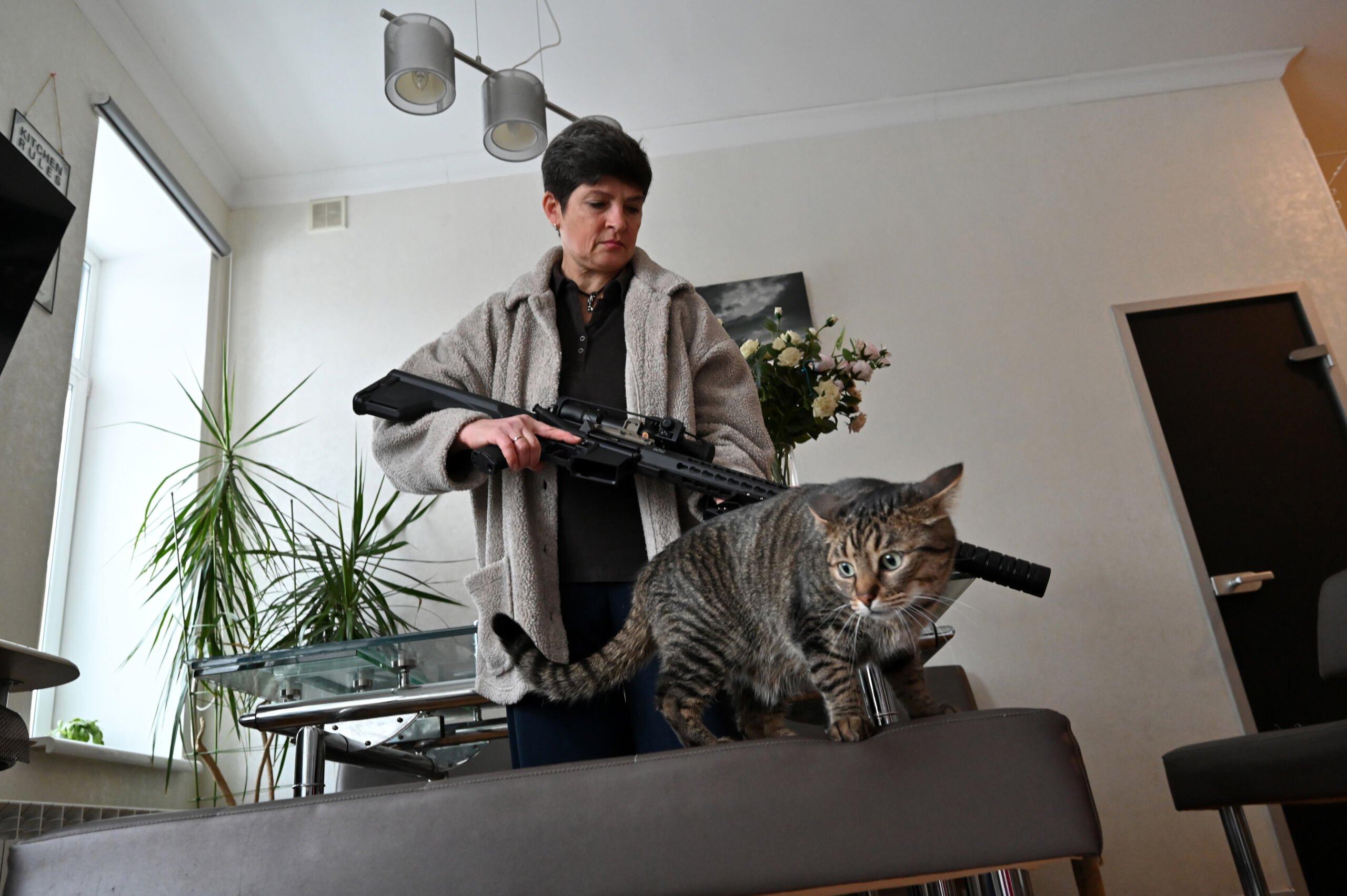 Kobieta w średnim wieku pokazuje długą broń. Na pierwszym planie - kot