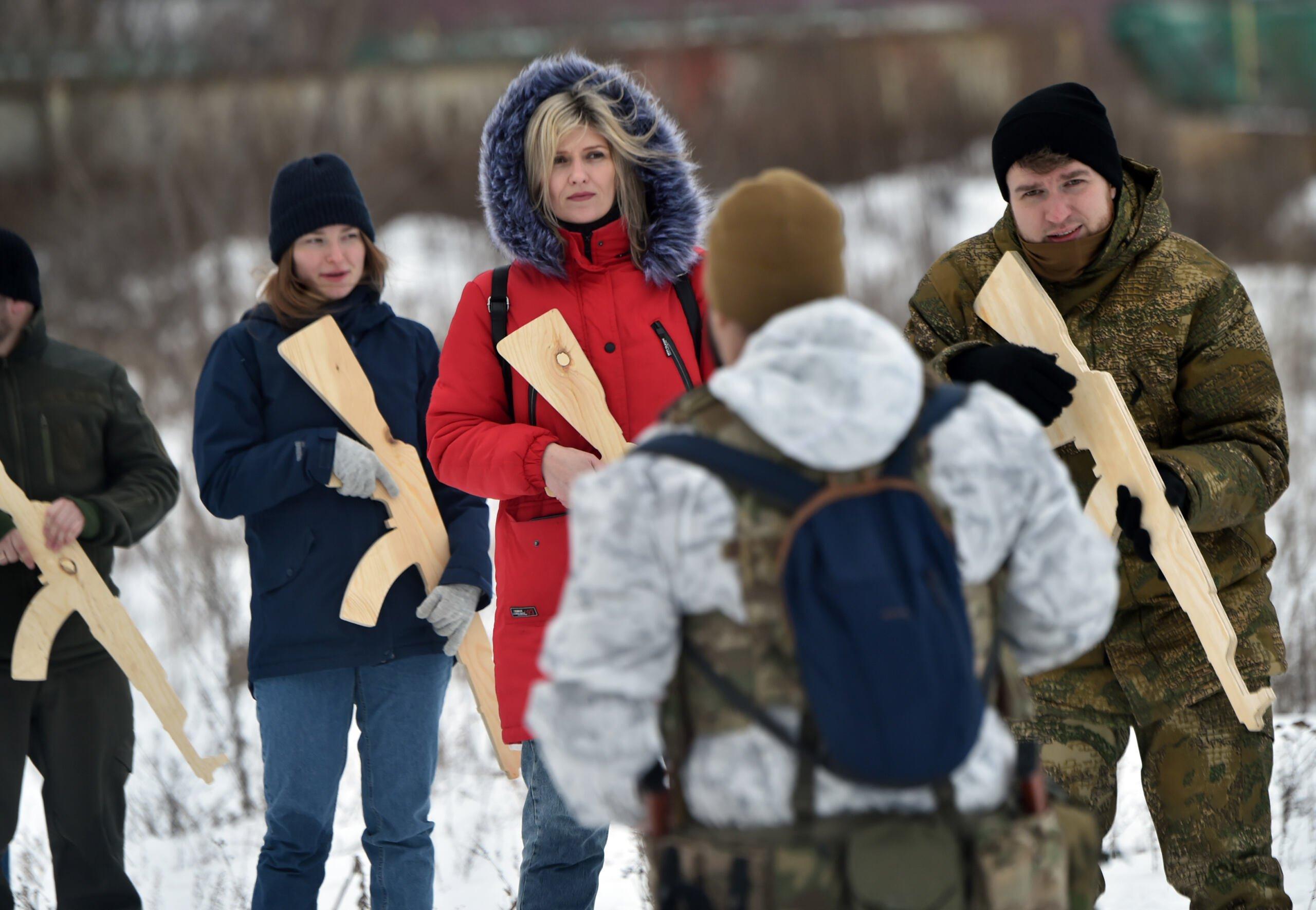 grupa cywilów, w tym kobiet, z drewnianymi atrapami karabinów ćwiczy pod okiem wojskowego instruktora w Kijowie