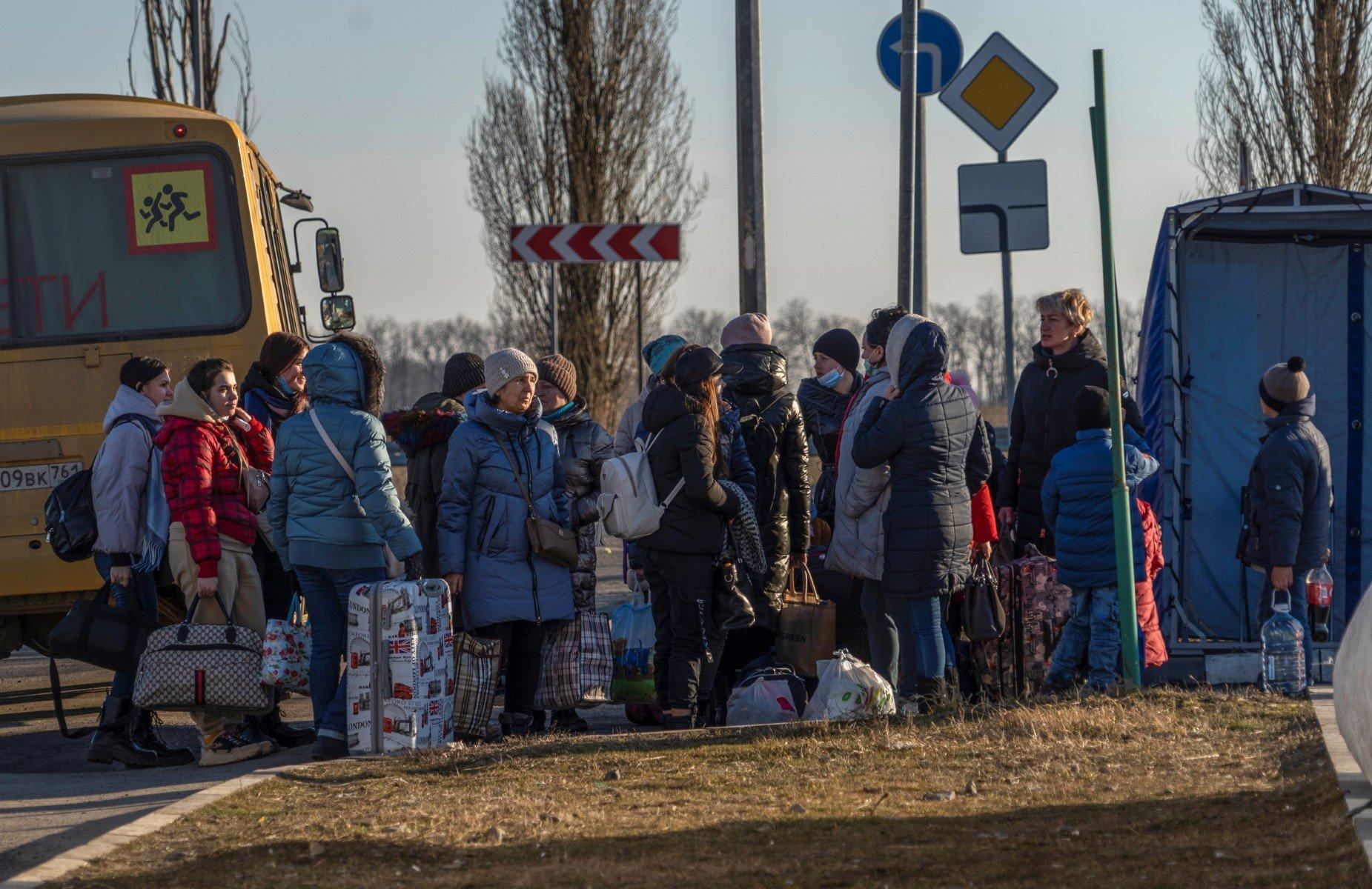 Ludzie w zimowych ubraniach z walizkami i tobołami obok autobusu do przewozu dzieci
