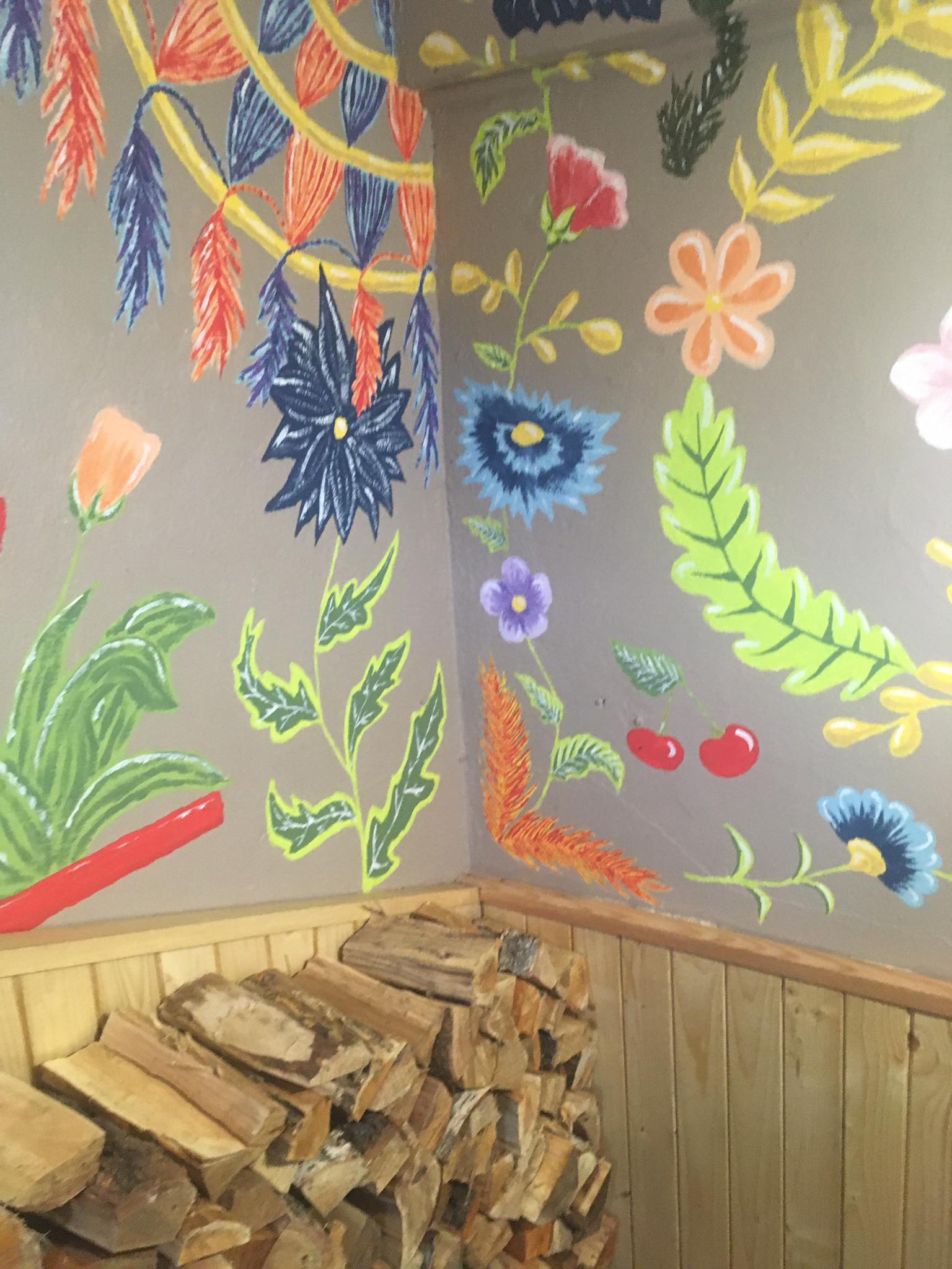 Sciany z namalowanymi kwiatami, pod ścianą drewniane polana