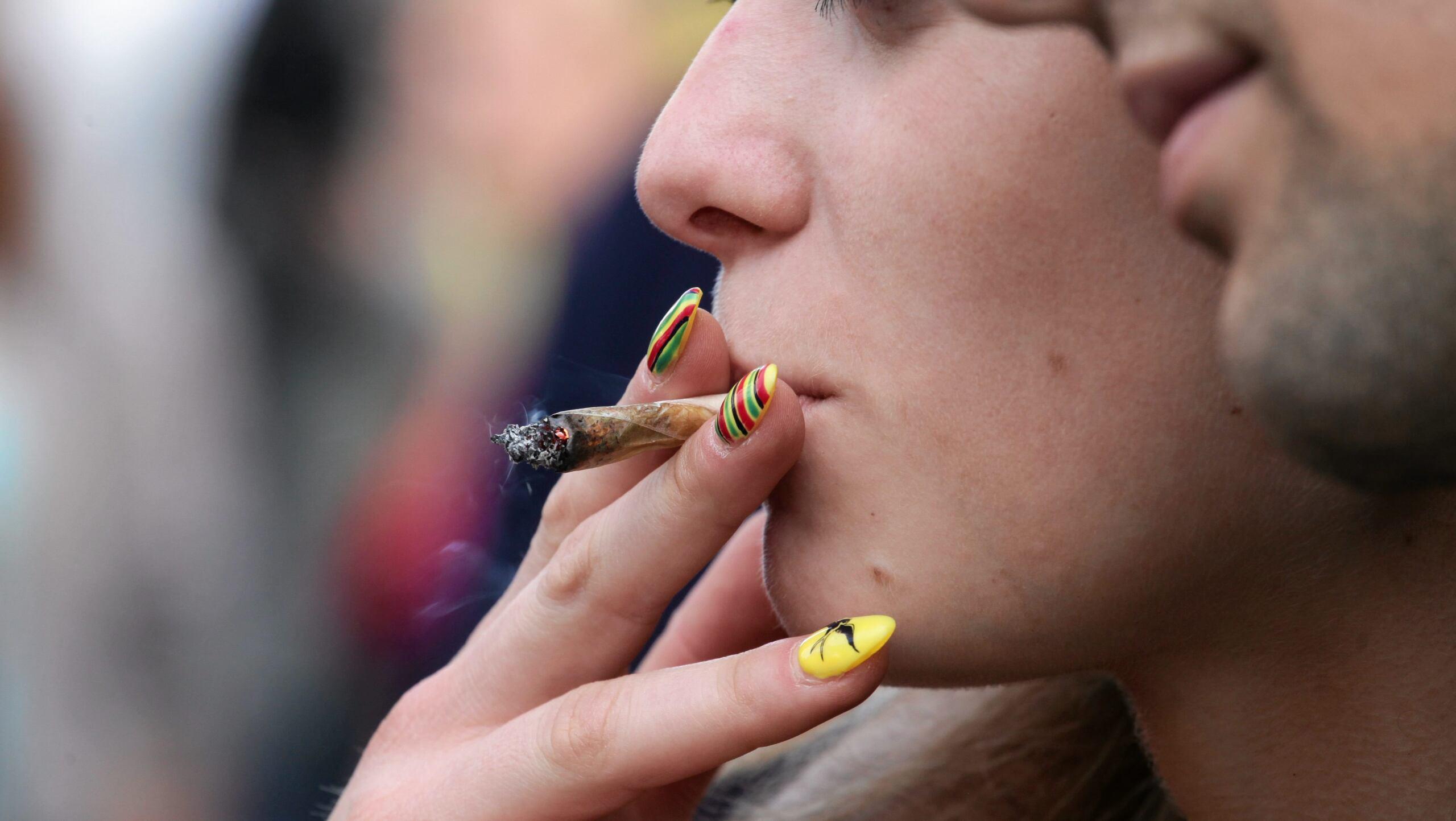 Skręt z marihuaną trzymany w ustach przez młodą kobietę z pomalowanymi paznokciami