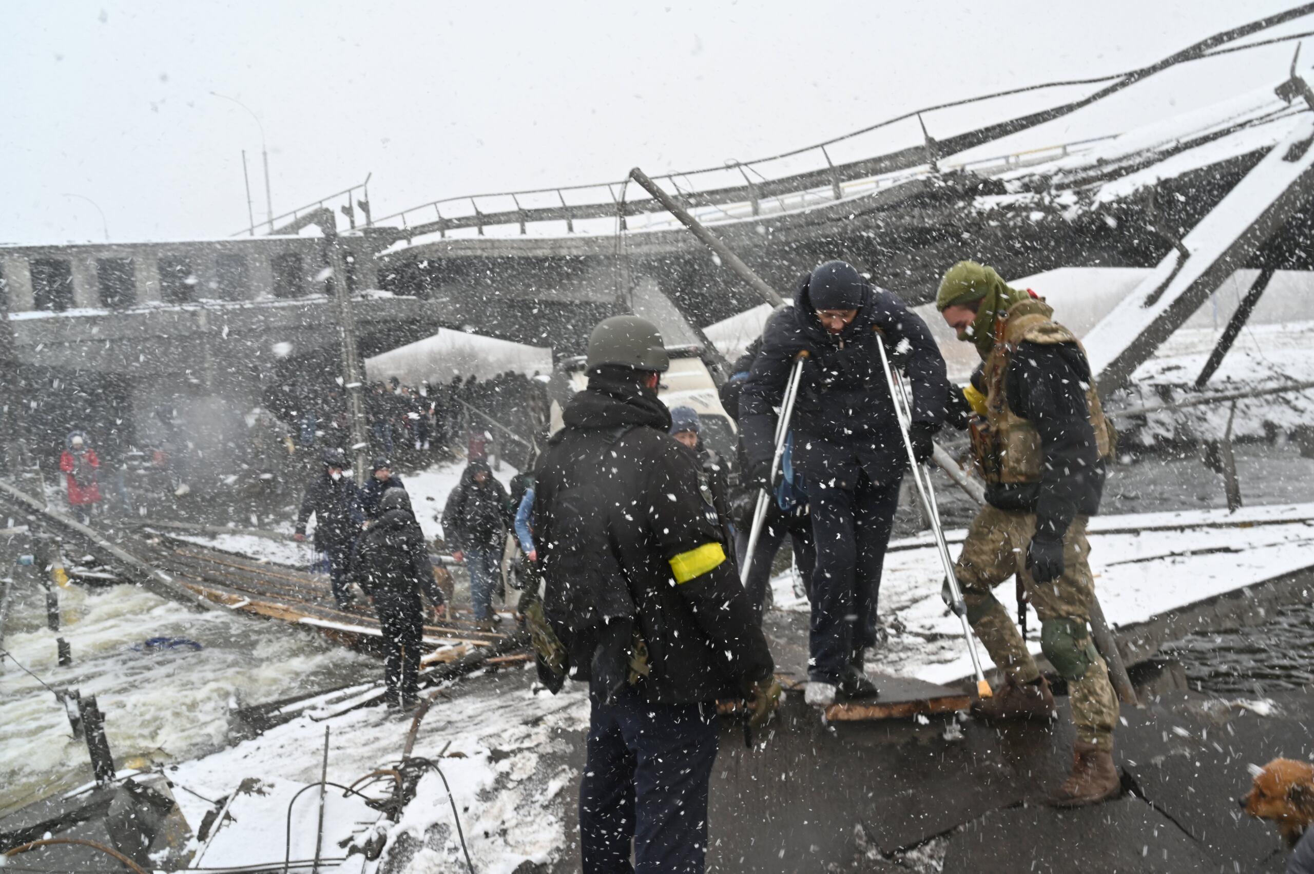 Żołnierze ukraińscy pomagają osobie o kulach przejść po zaimprowizowanym moście
