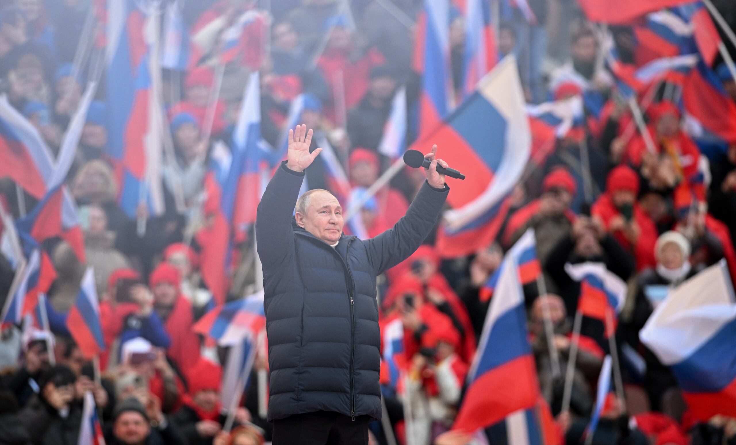 Putin wznosi ręce do góry, w tle - tlum z rosyjskimi flagami na widowni stadionu