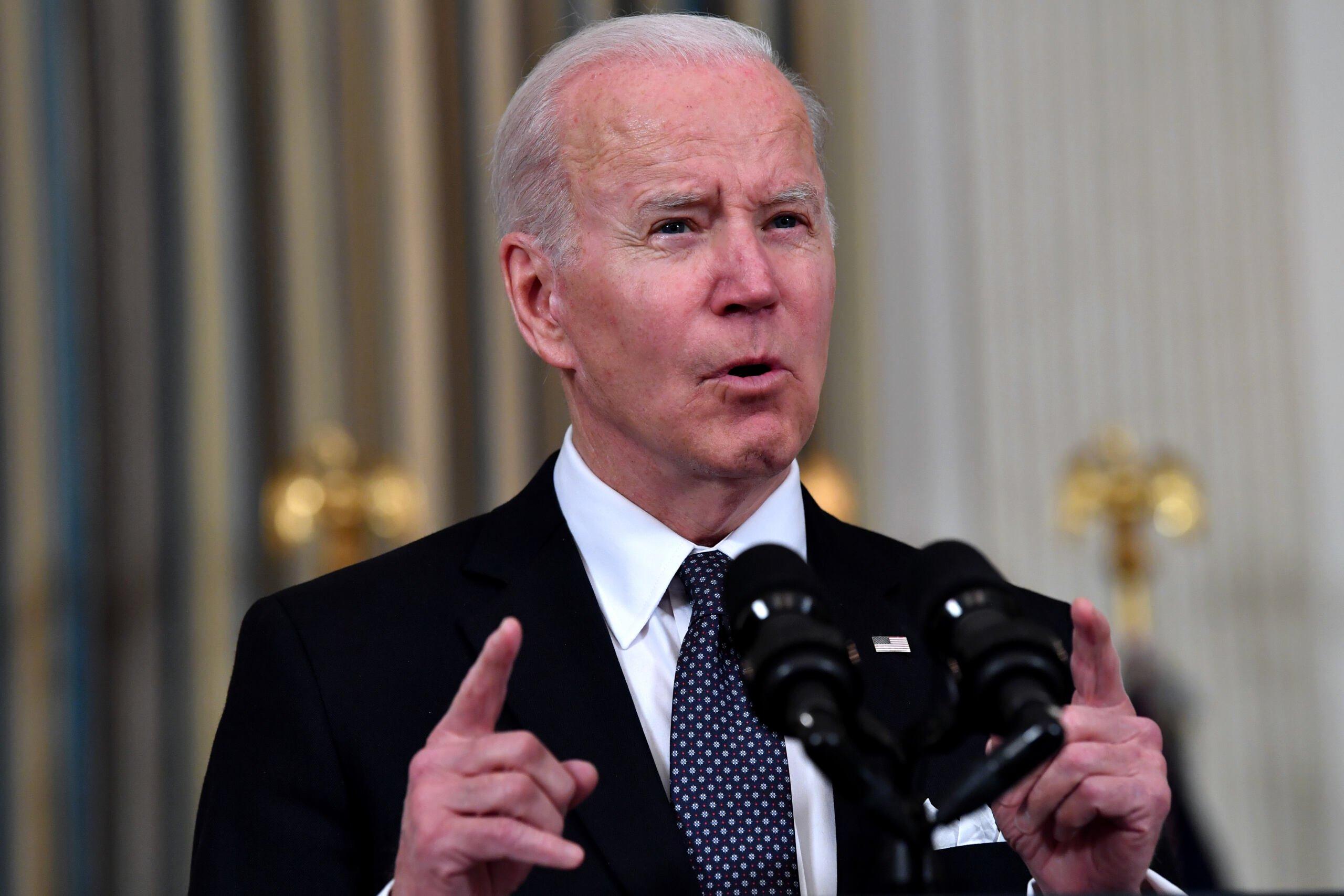 Joe Biden, mężczyzna, starszy, stoi prze mikrofonem i trzyma uniesioną rękę