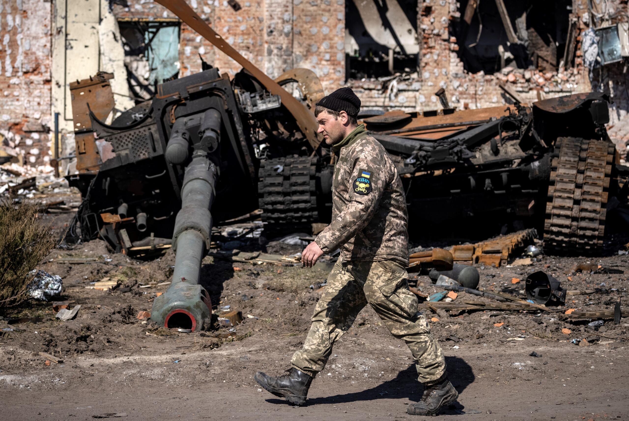 Żołnierz z emblematem Ukrainy na ramieniu, w tle - zniszczone rosyjskie czołgi