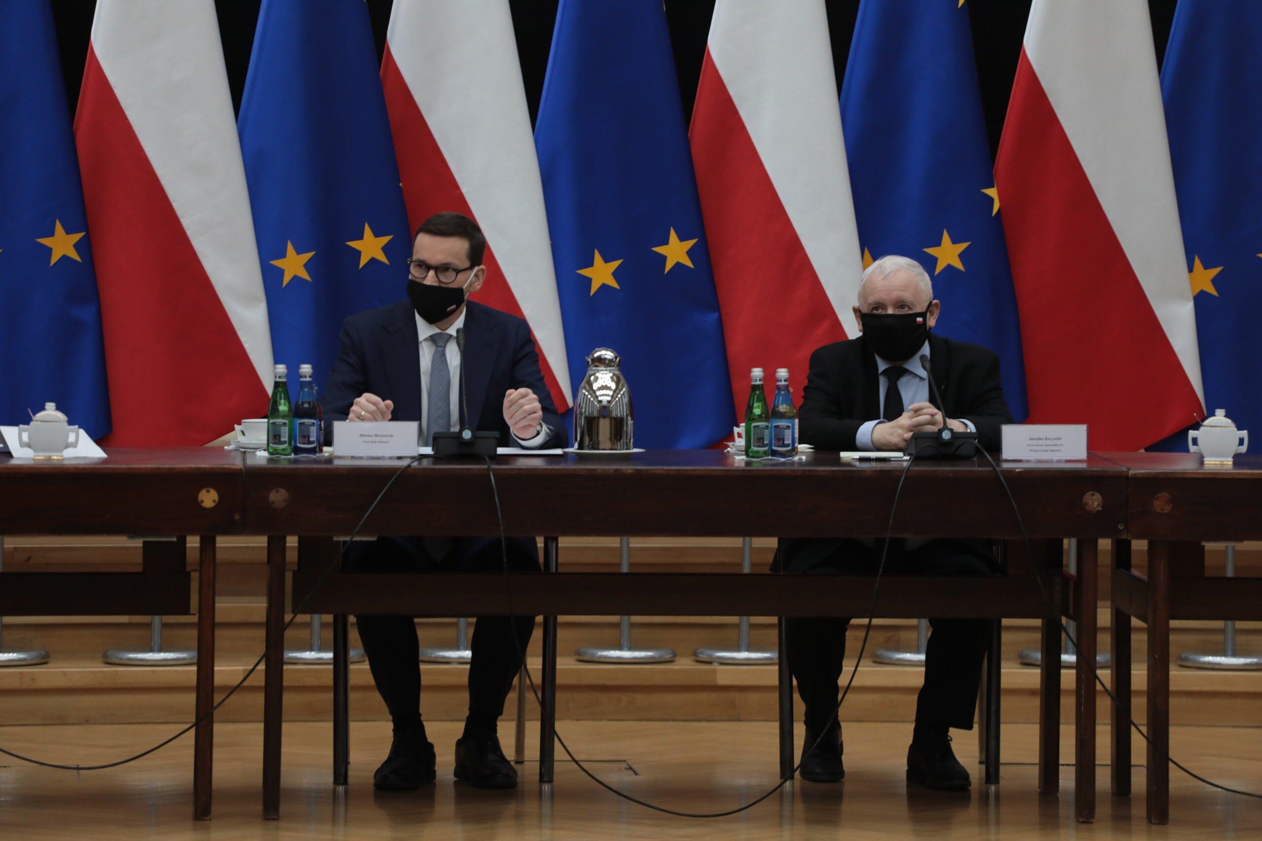 Mateusz Morawiecki i Jarosław Kaczyński siedzą przy stole, w tle flagi Polski i Unii Europejskiej