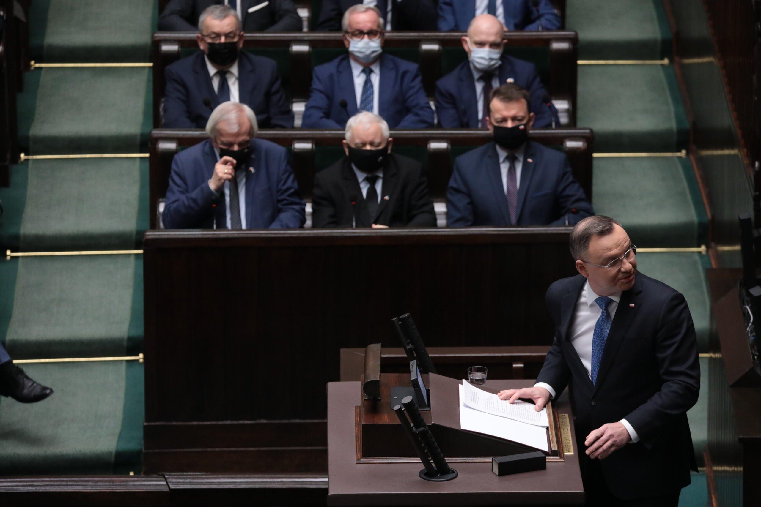 Prezydent Duda na mównicy sejmowej podczas obrad Zgromadzenia Narodowego. W tle prezes PiS Jarosław Kaczyński