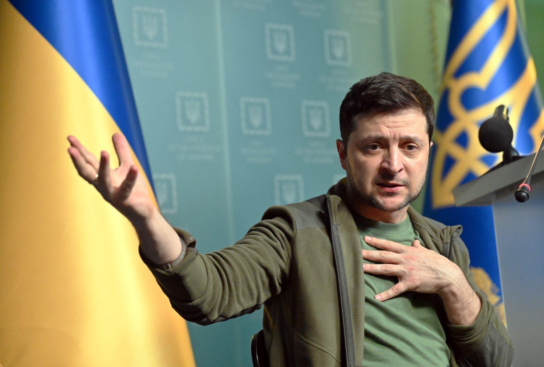 Wołodymyr Zełenski z wyciągniętą prawą ręką i lewą przyciśniętą do piersi