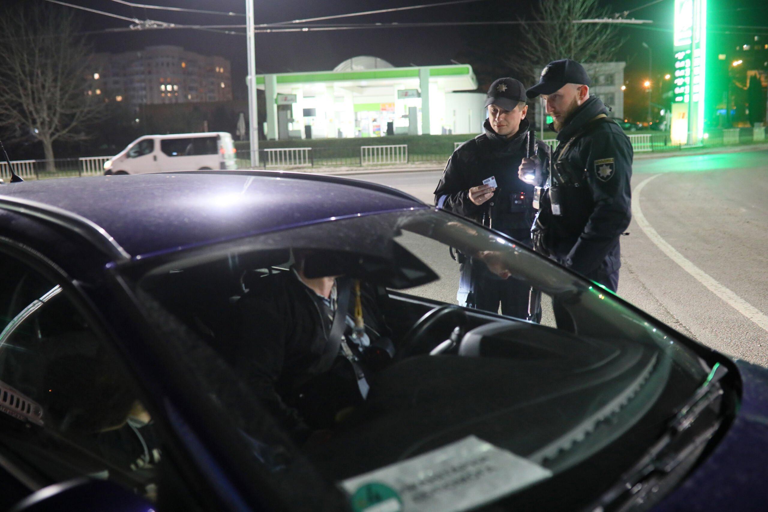 Dwóch policjantów dokonuje kontroli osoby w samochodzie osobowym we Lwowie, wieczorem