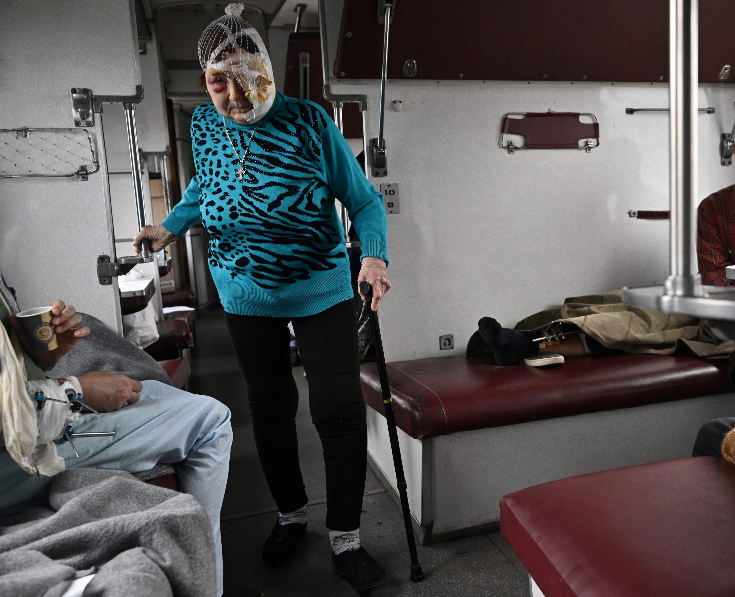 Starsza kobieta z zabandażowaną głową idzie o lasce przez medyczny pociąg ewakuujący chorych i rannych na zachód Ukrainy.