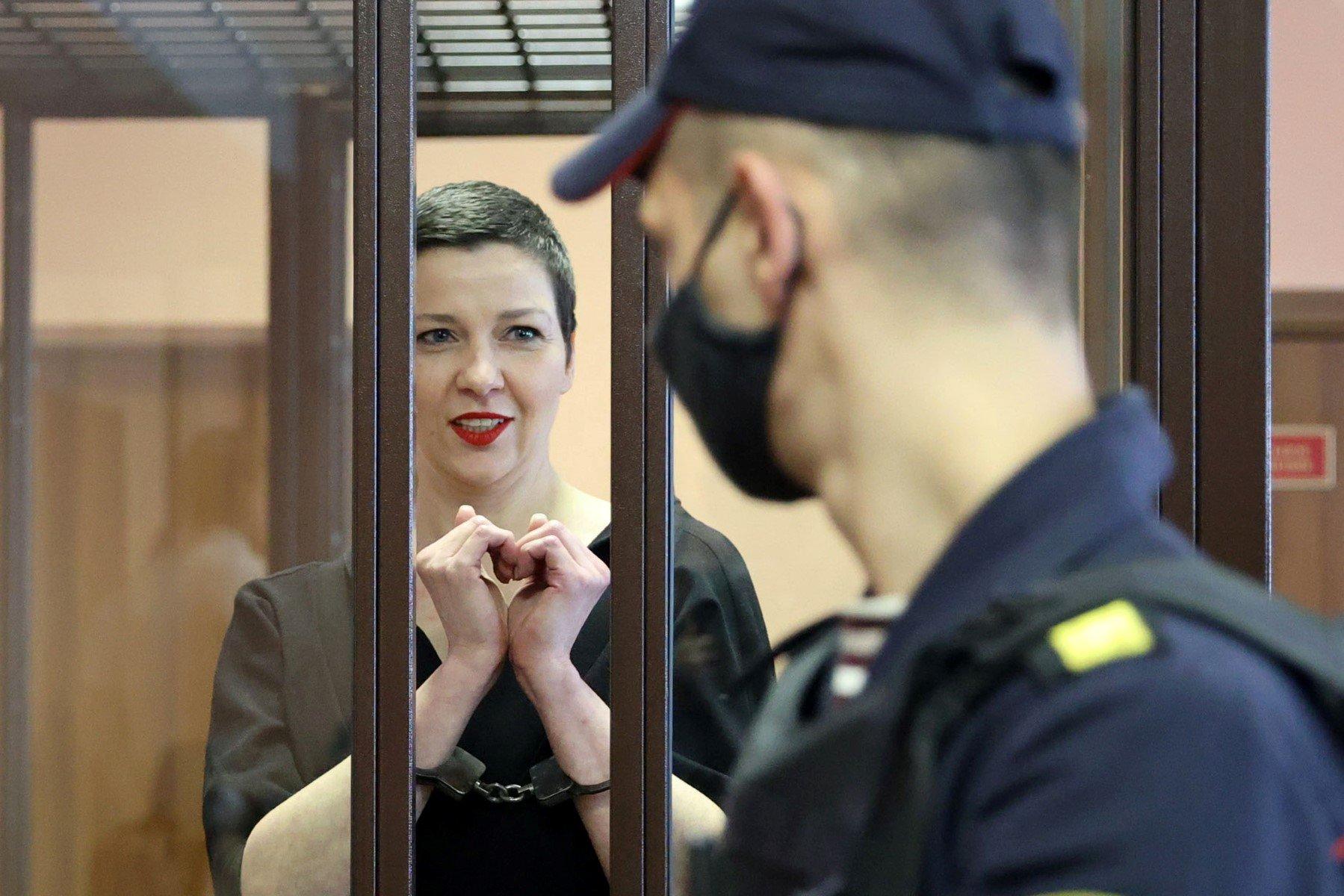 Maria Kalesnikawa krótko ostrzyżona zza krat pokazuje złożonymi dłoniami znak serca, na pierwszym plane profiol strażnika w masce