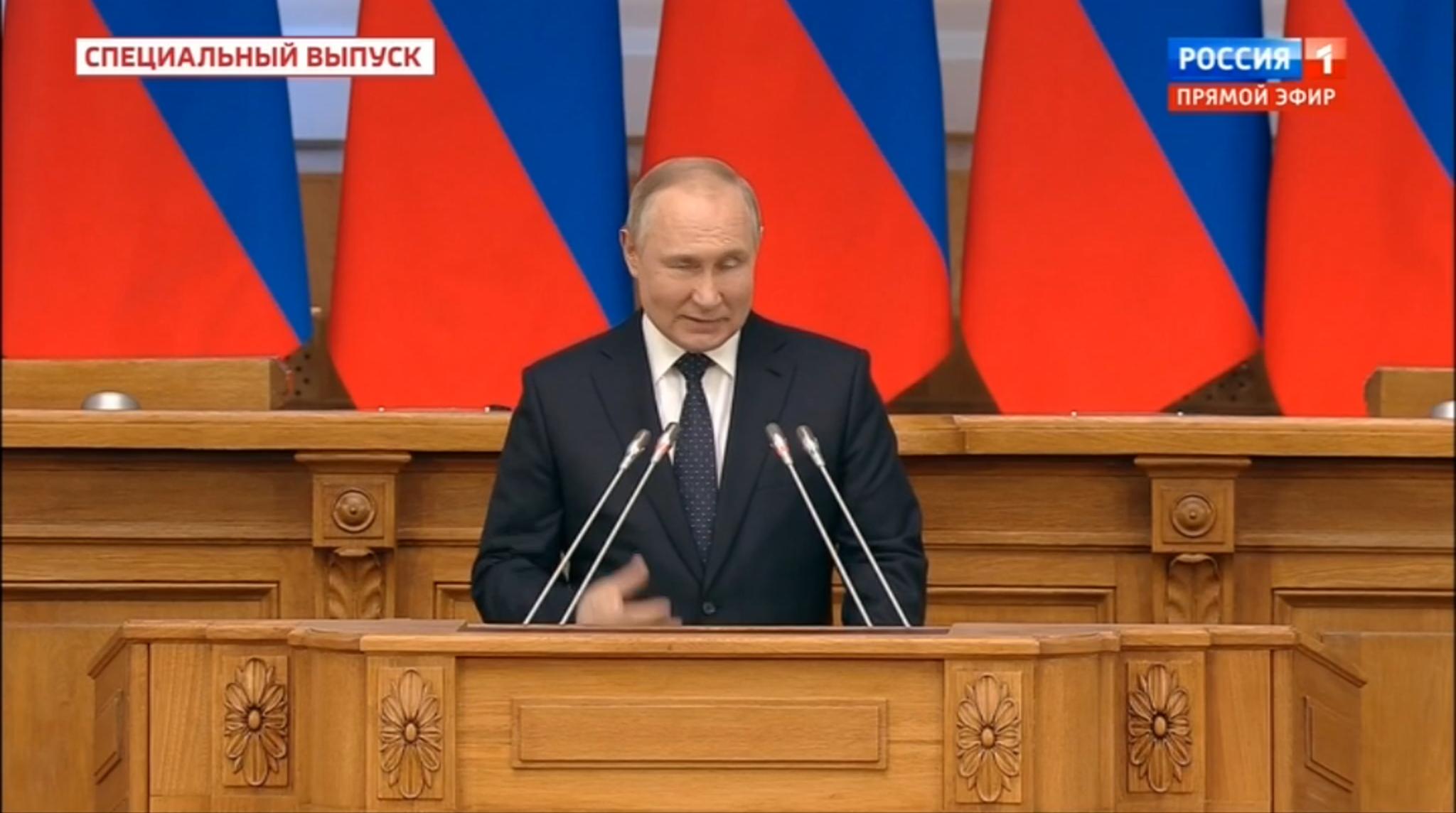 Mężczyzna (Putin) przemawia gestykulując i mrużąc oko