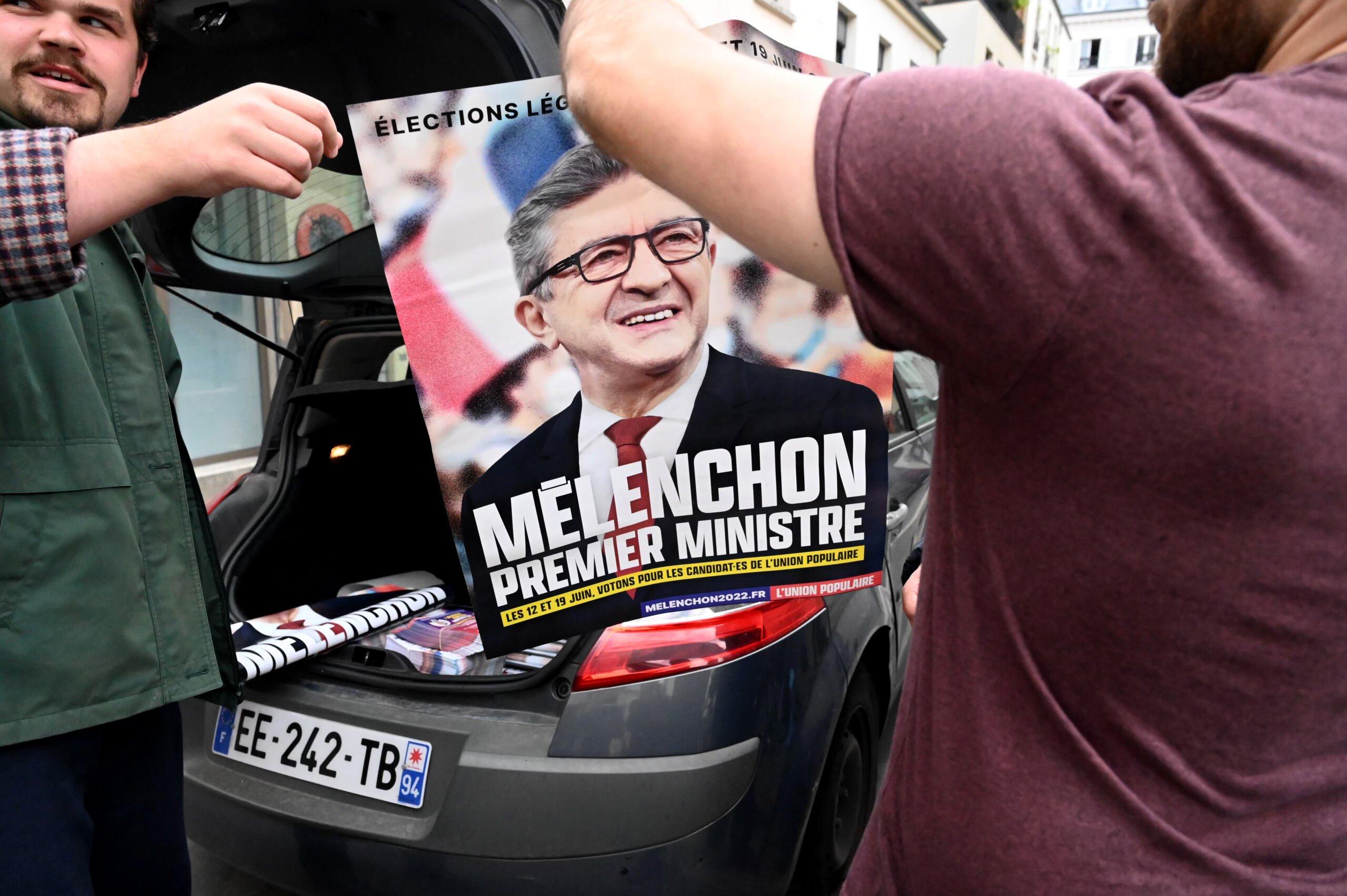 Dwóch mężczyzn wychodzących poza kadr trzyma plakat z Mèlenchonem