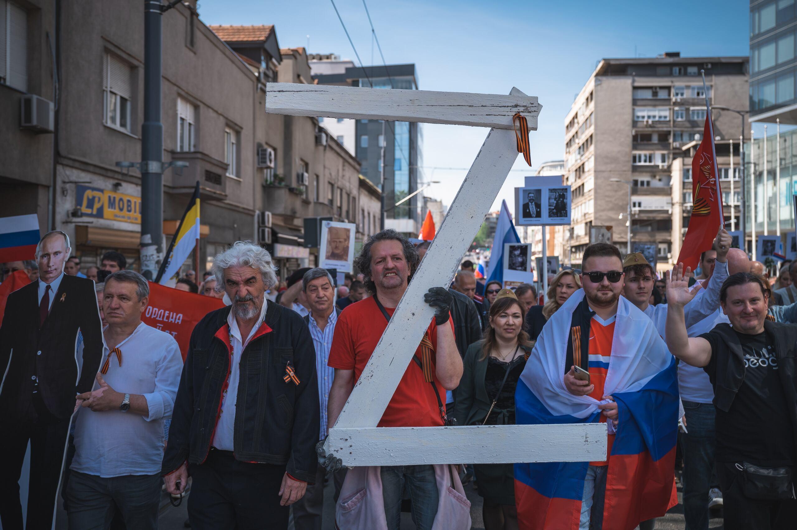mężczyźni owinięty serbskimi flagami niosą wielką literę Z