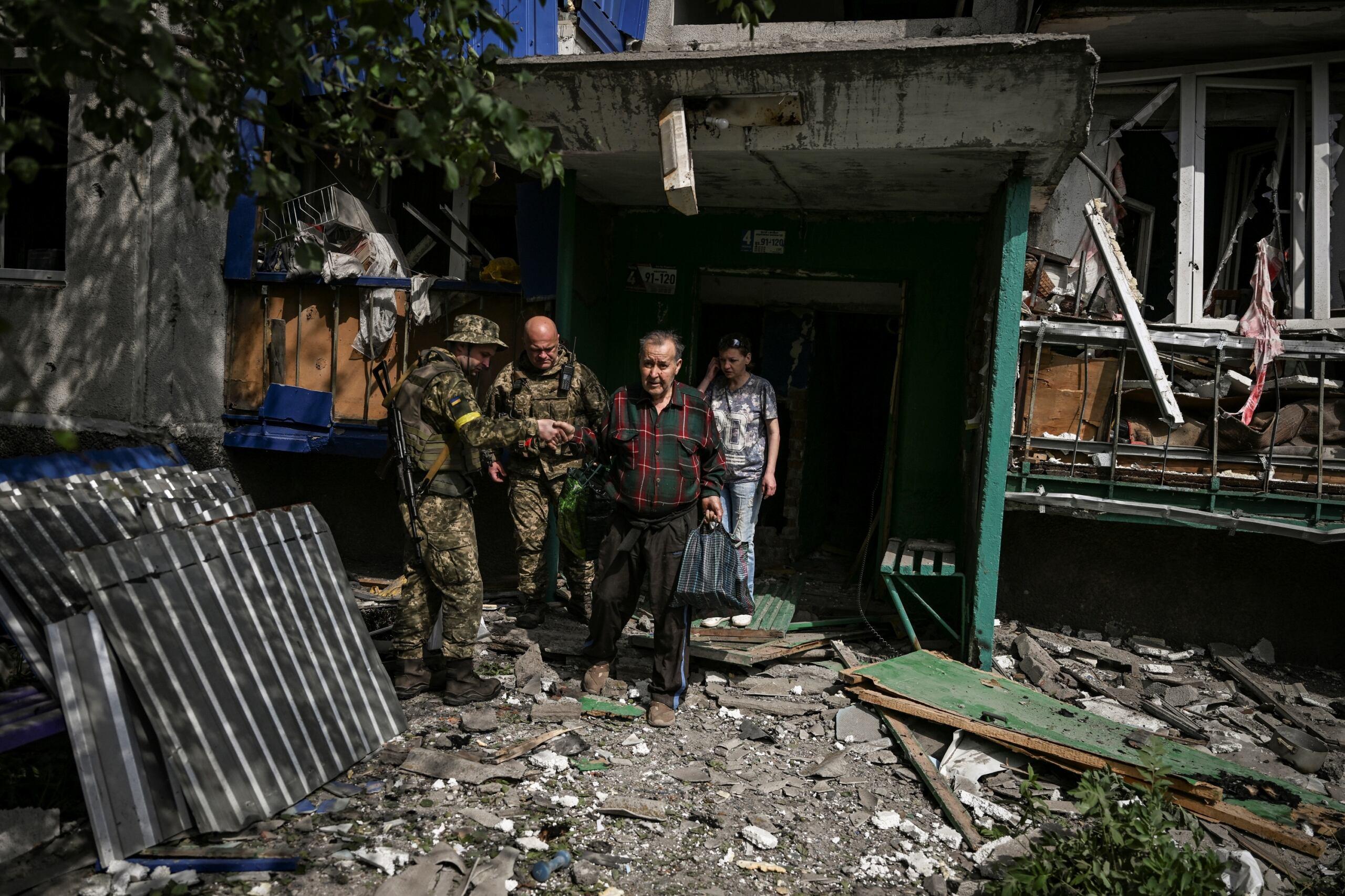 żołnierze pomagają starszemu mężczyznie wyjść ze zbombardowanego domu