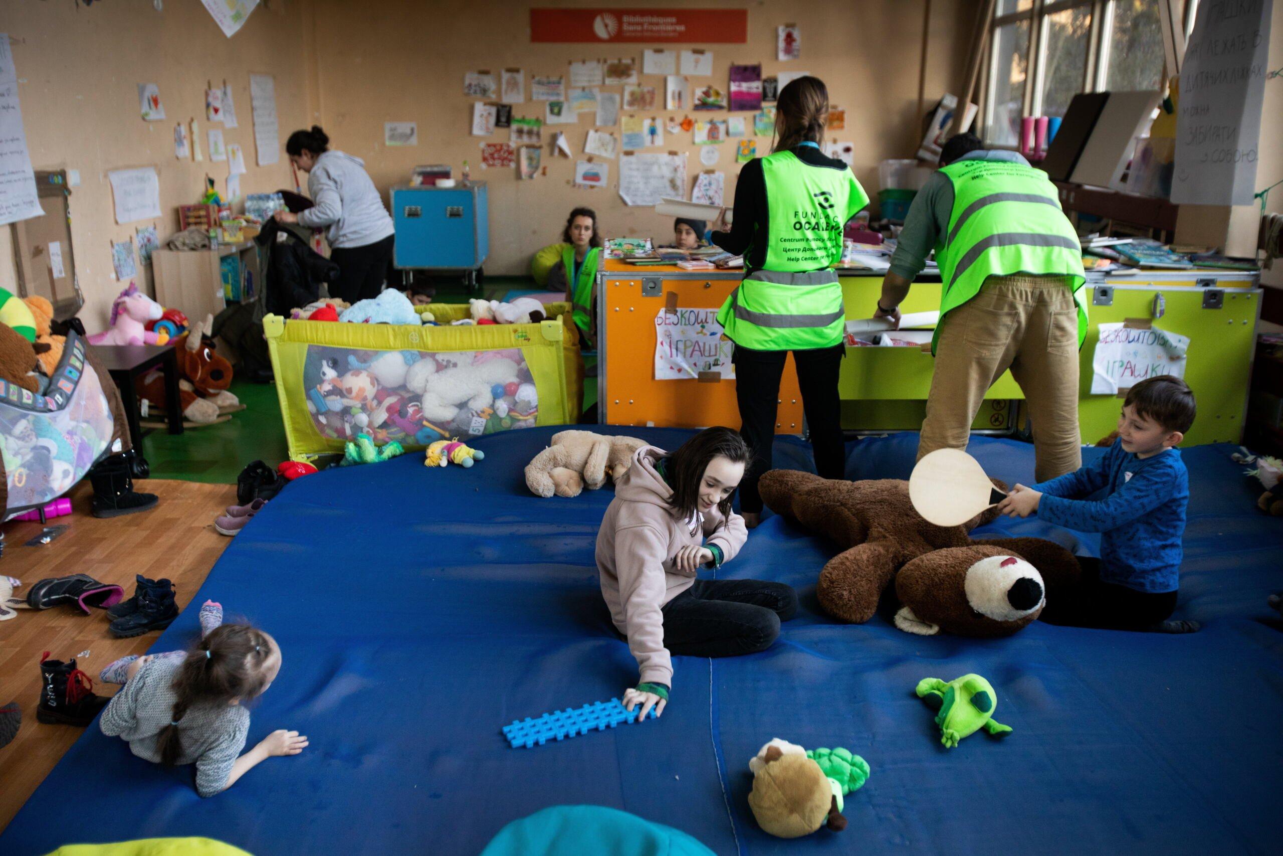 Dzieci bawią się na podłodze, obok wolontariusze w kamizelkach z napisem Fundacja Ocalenie
