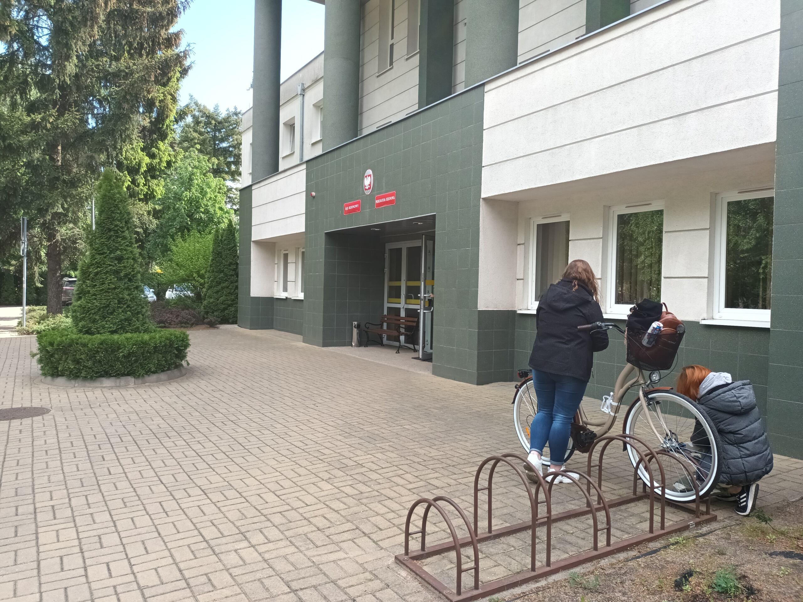 Dwie kobiety odpinają rower pod budynkiem sądu
