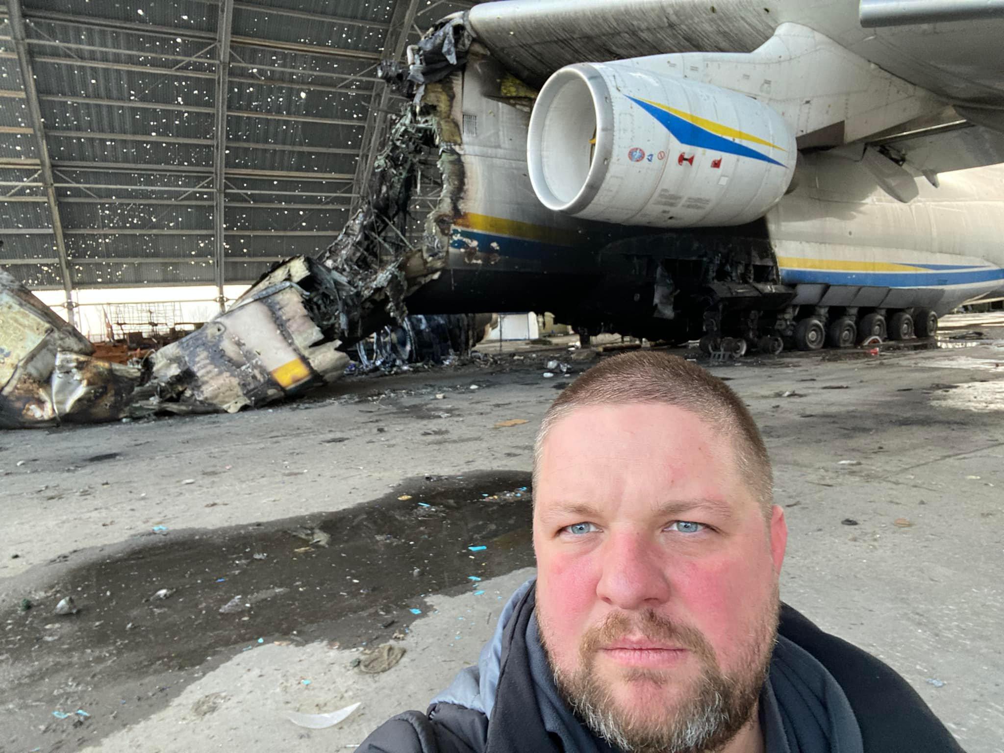 Mężczyzna fotografuje się na tle zniszczonego samolotu transportowego Mrija