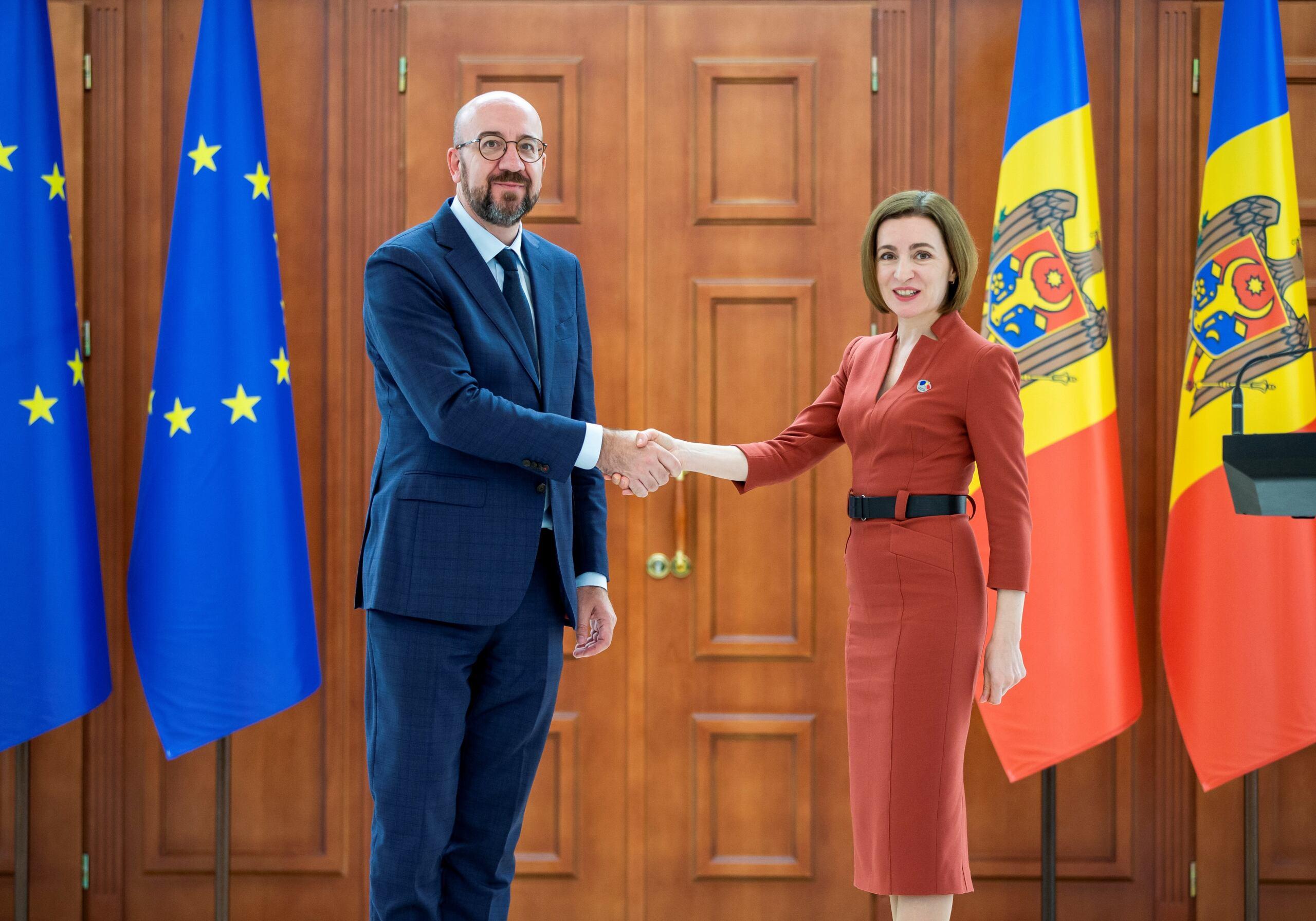 Ubrany w garnitur szef Rady Europejskiej Charles Michel wita się z ubraną ciemno czerwoną sukienkę prezydentkę Mołdawii Maię Sandu. W tle flagi UE i Mołdawii