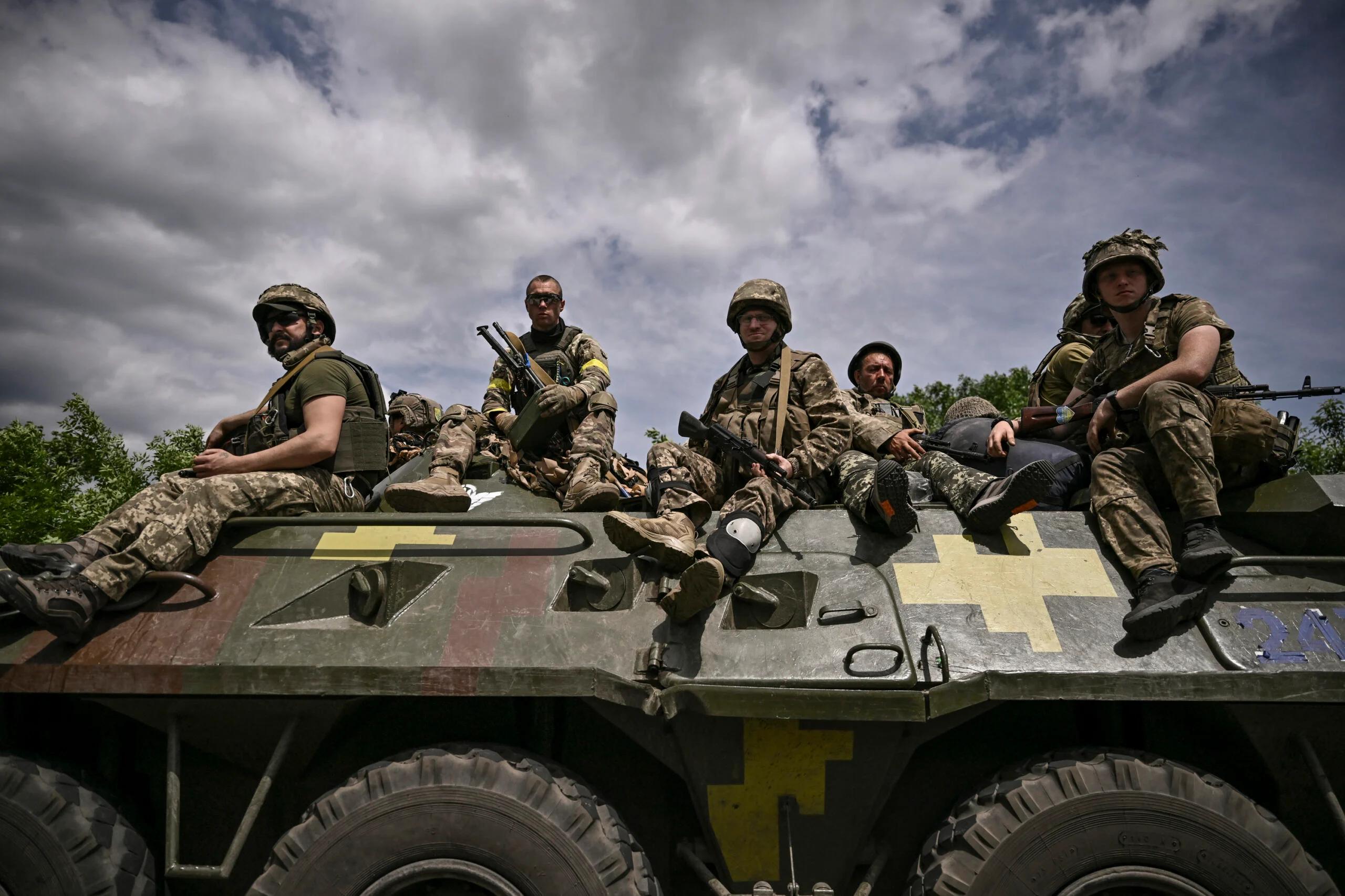 Żołnierze z żółtymi opaskami siedzą na wozie bojowym