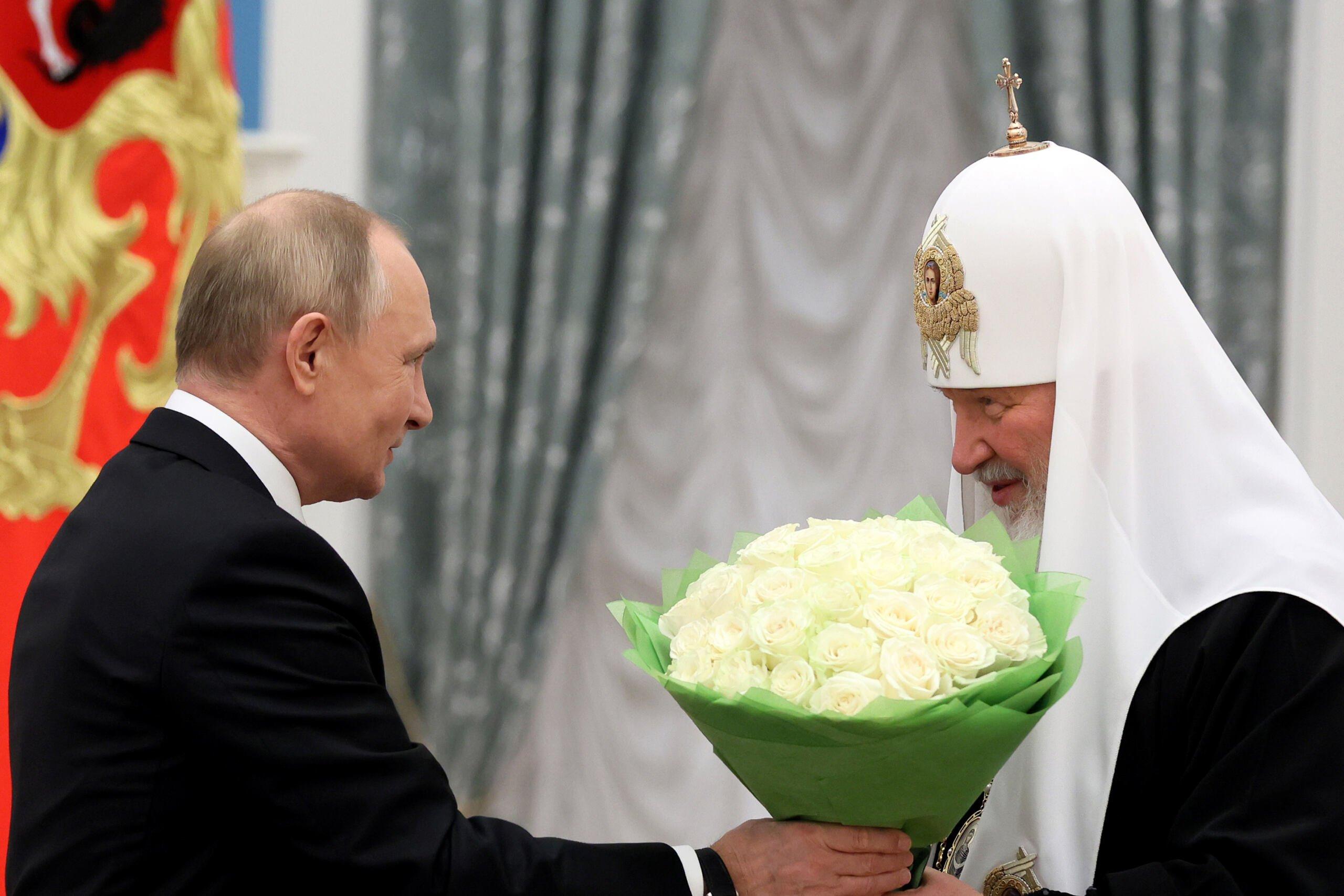 Prezydent Rosji Władimir Putin we wnętrzach Kremla wręcza białe kwiaty patriarsze Cyrylowi