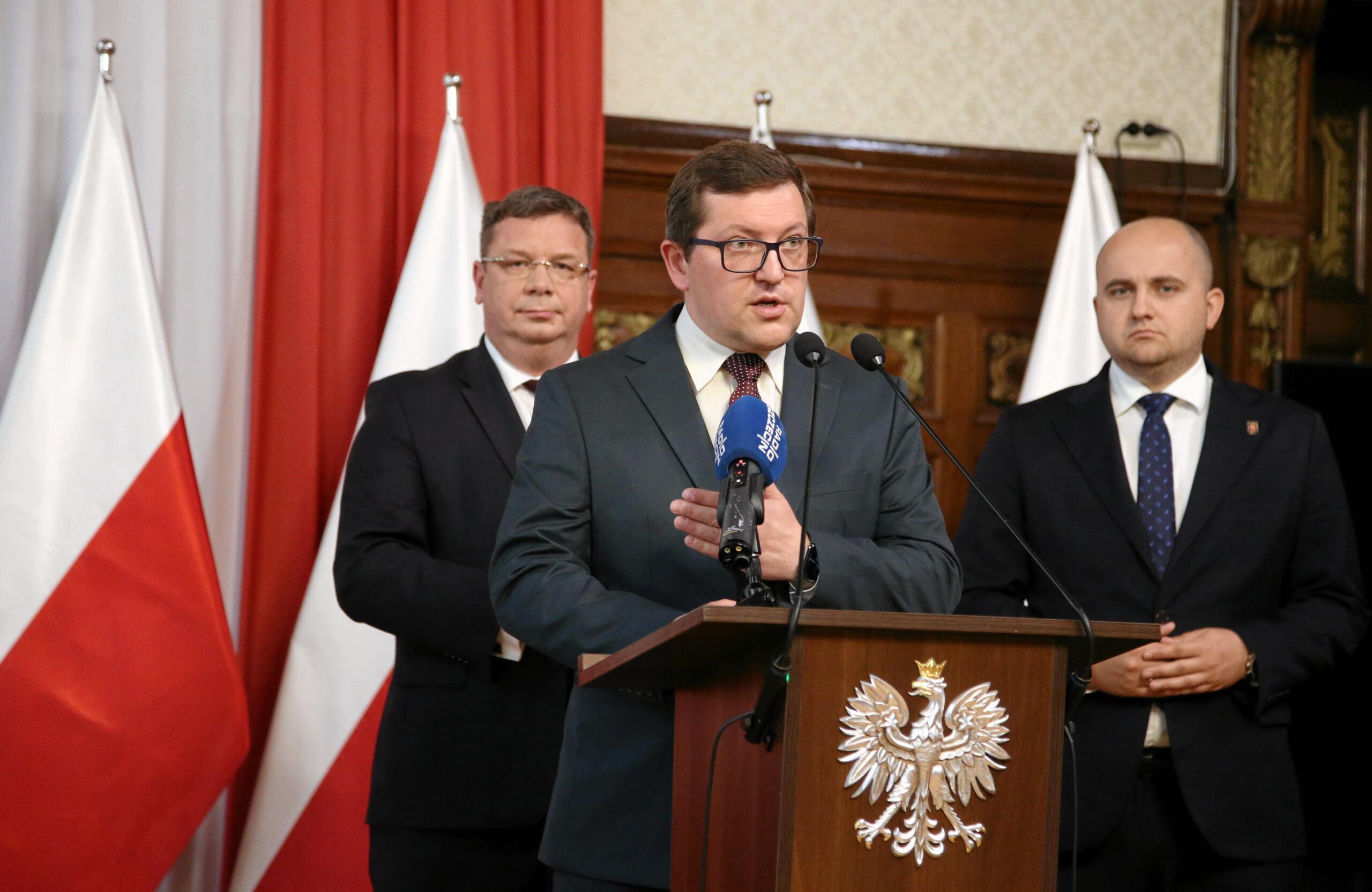 Mateusz Wagemann w stoi przy mównicy w towarzystwie Dariusza Mateckiego i Michała Wójcika z Solidarnej Polski