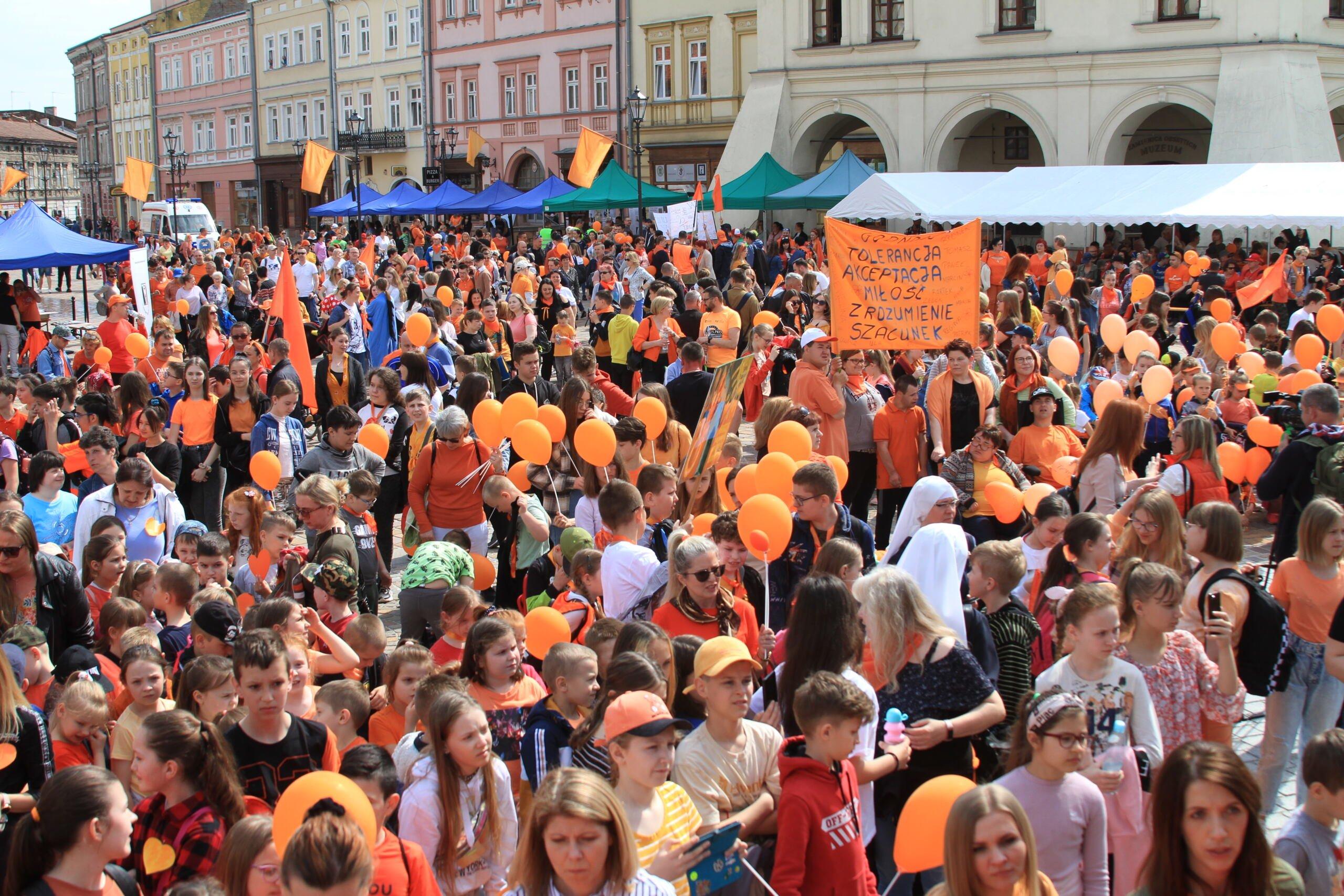 Tłum ludzi, w tym dzieci, z pomarańczowymi balonikami. W tle zabytkowe kamienice
