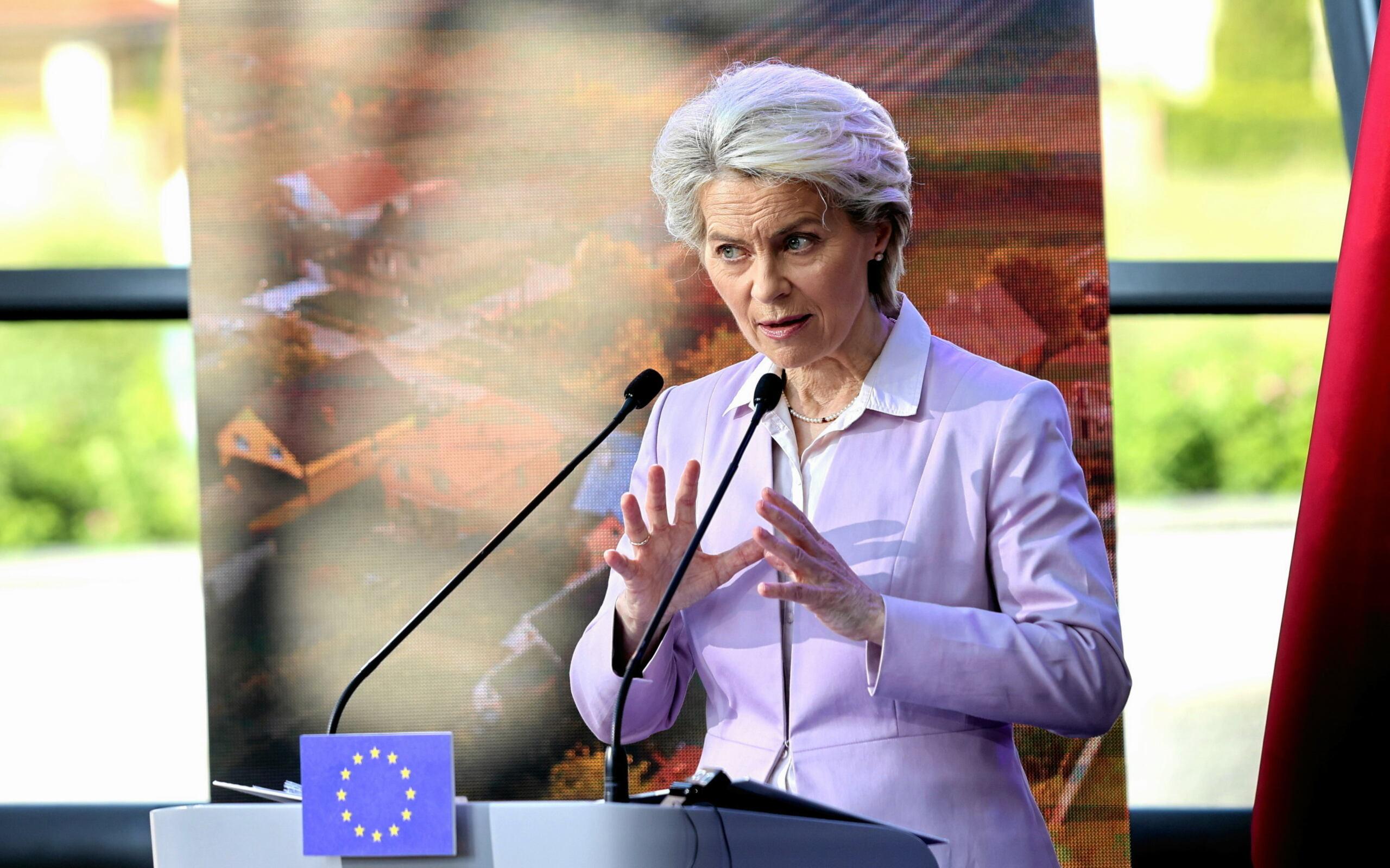 Ursula von der Leyen w jasnym żakiecie wygłasza oświadczenie podczas wizyty w Polsce. Na mównicy flaga Unii Europejskiej