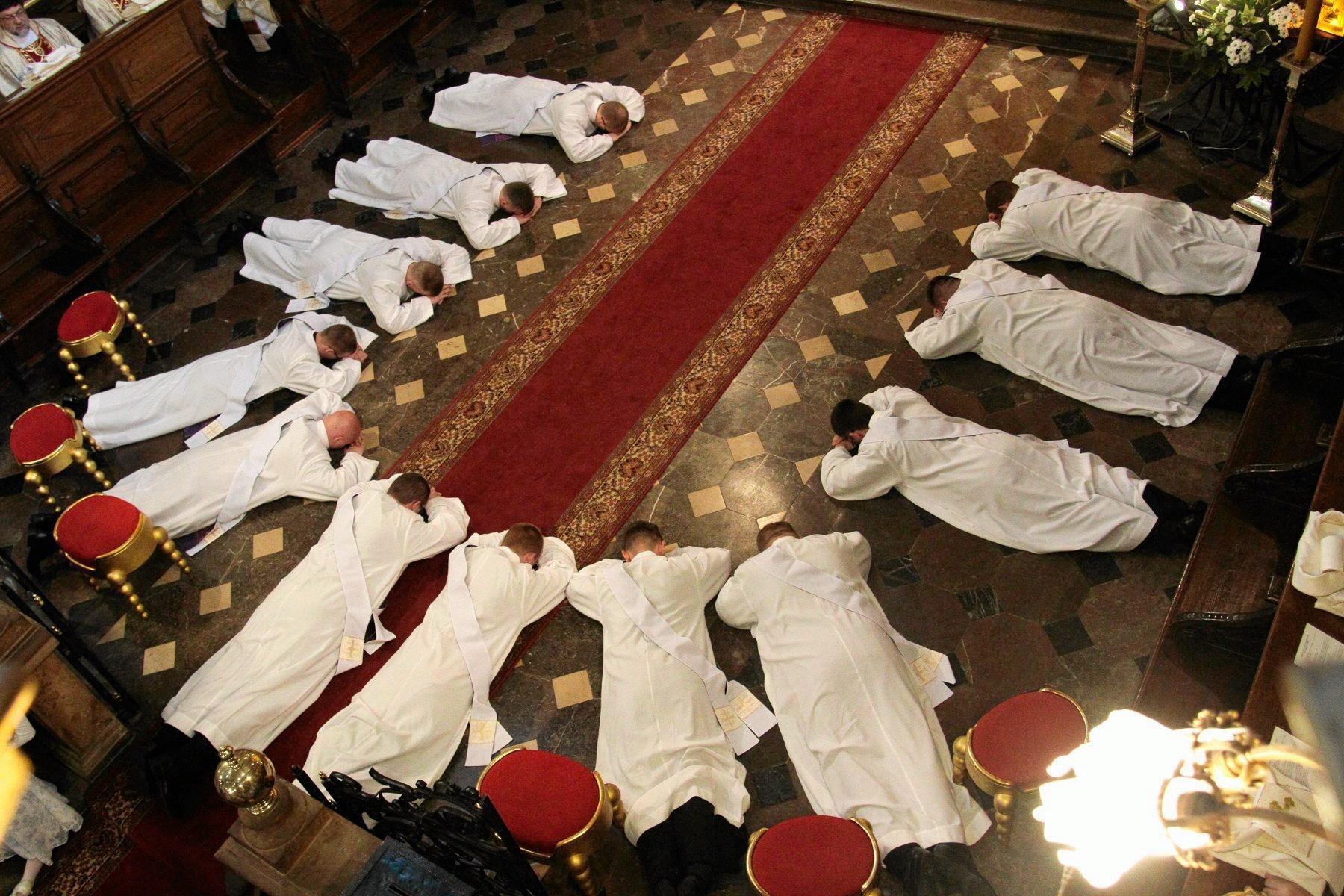klerycy w albach leżący na posadzce kościoła układający się w kształt litery U