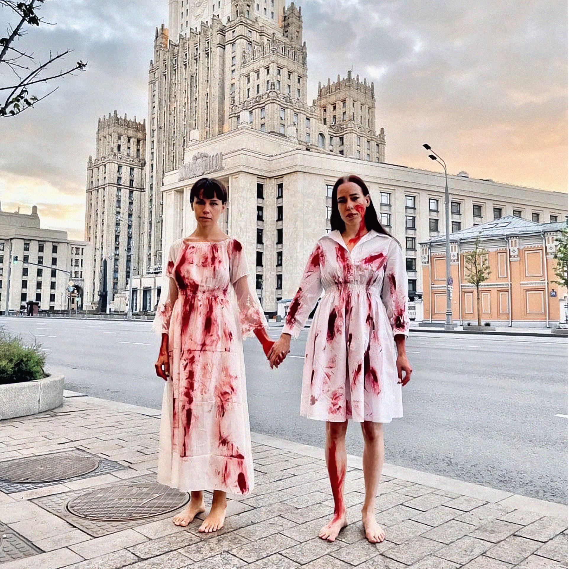 Dwie kobiety w białych sukniach poplamionych czerwoną farbą, jakby krwią