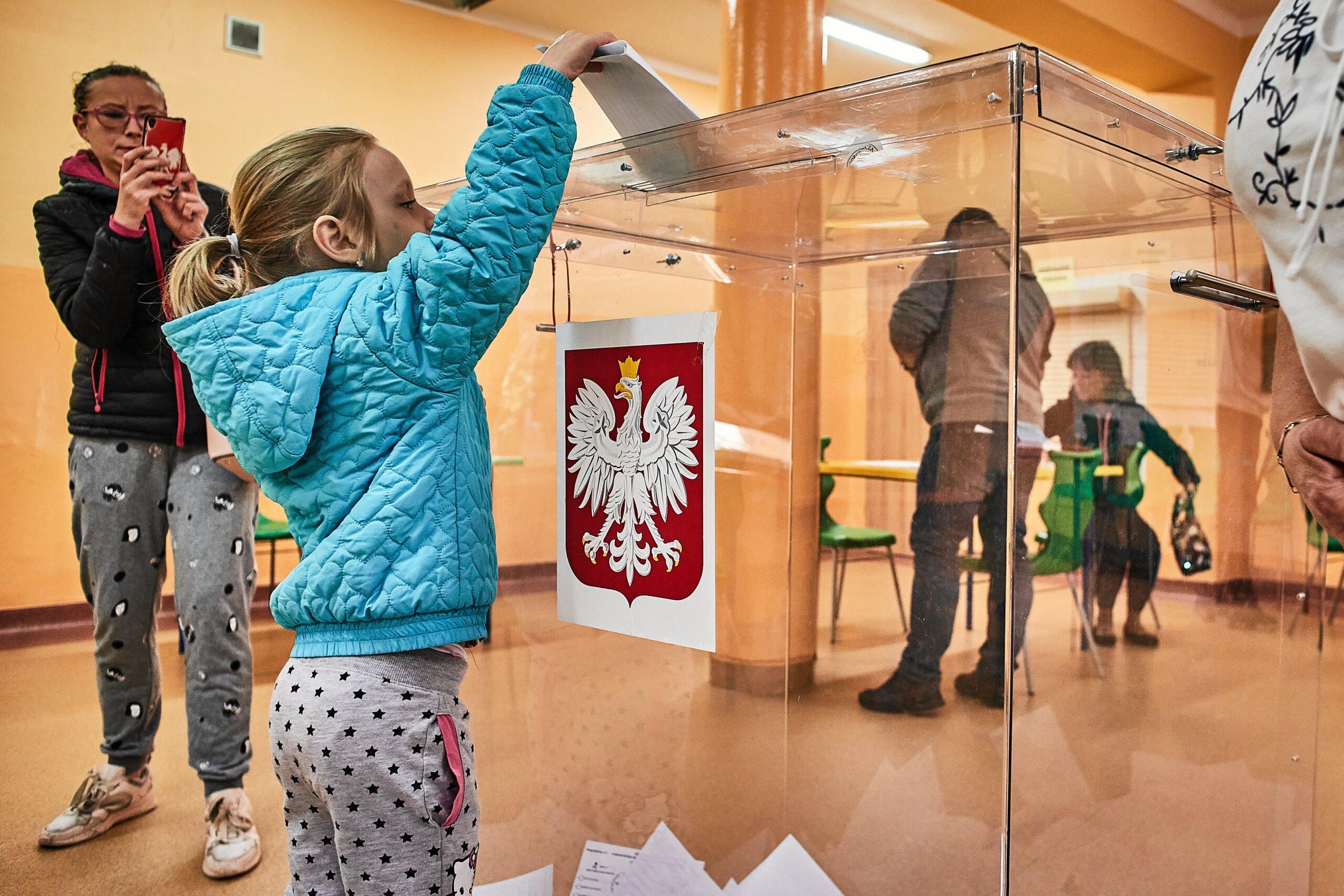 Dziewczynka wspina się na palce, żeby wrzucić głos do urny wyborczej