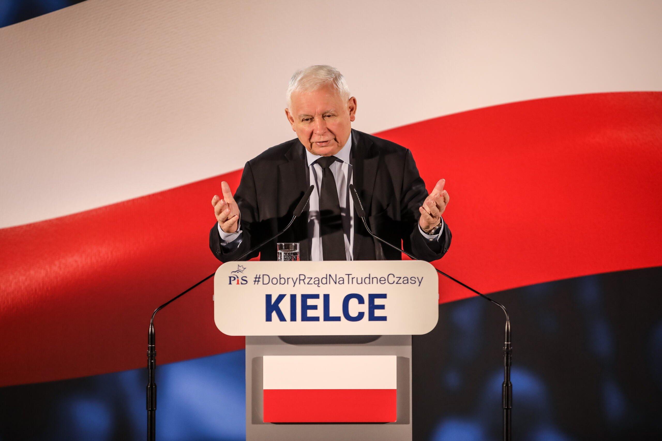 Jarosław Kaczyński przemawia na tle biało-czerwonej flagi