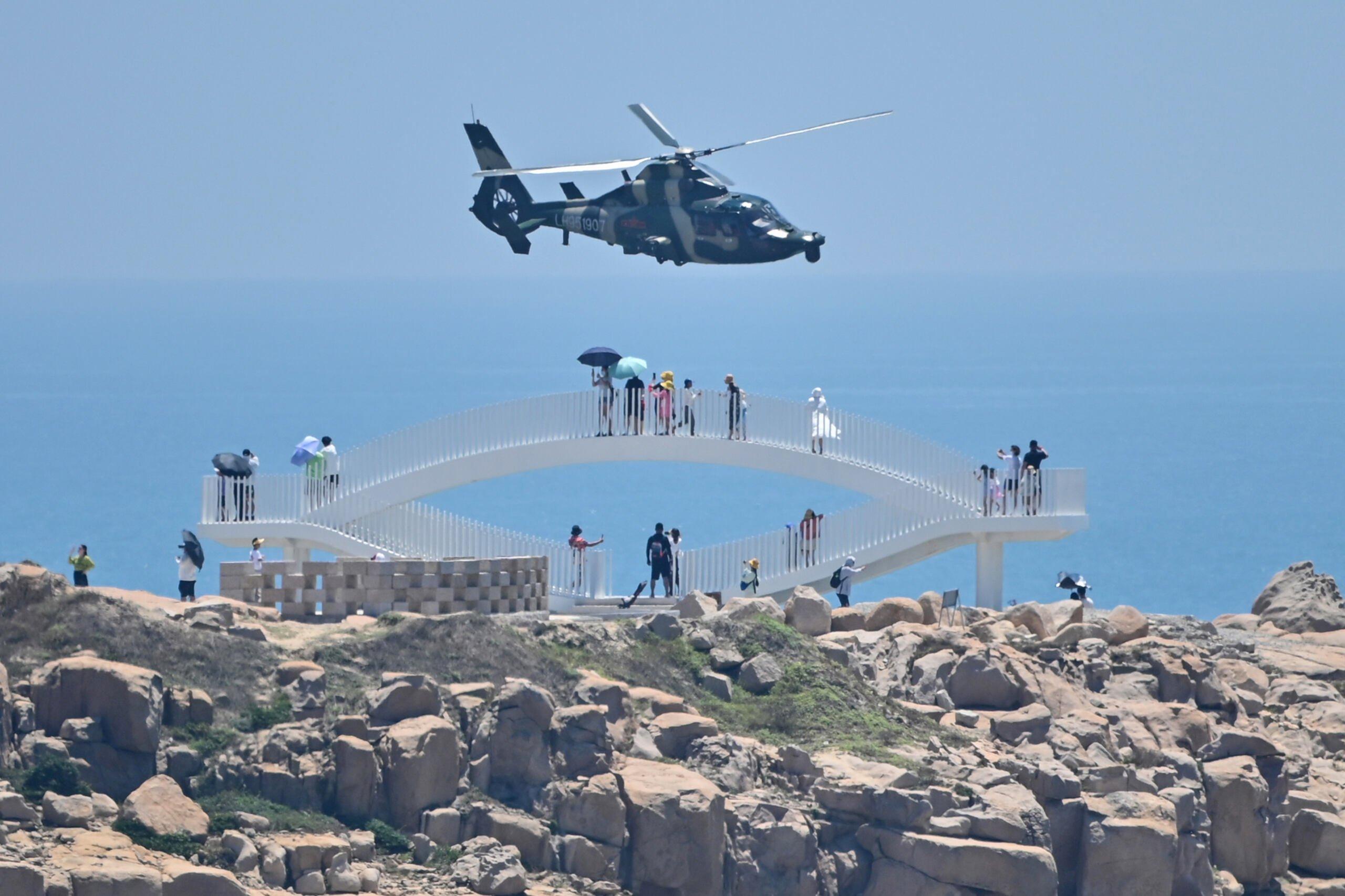 Tourists look on as a Chinese military helicopter flies past Pingtan island, one of mainland China's closest point from Taiwan, in Fujian province on August 4, 2022, ahead of massive military drills off Taiwan following US House Speaker Nancy Pelosi's visit to the self-ruled island. - China is due on August 4 to kick off its largest-ever military exercises encircling Taiwan, in a show of force straddling vital international shipping lanes following a visit to the self-ruled island by US House Speaker Nancy Pelosi. (Photo by Hector RETAMAL / AFP)