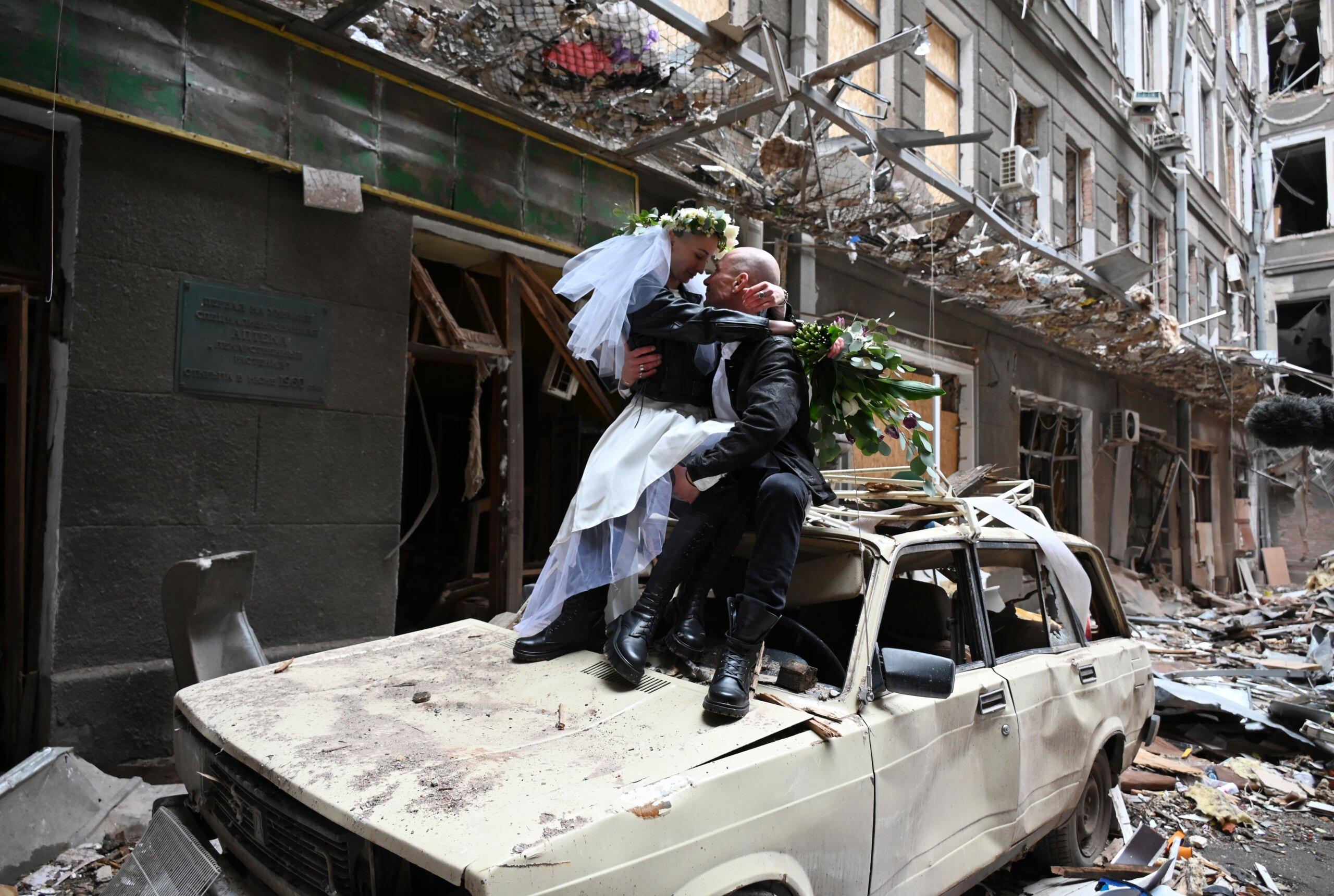 nowożeńcy pozują na wraku samochodu w zbombardowanym budynku