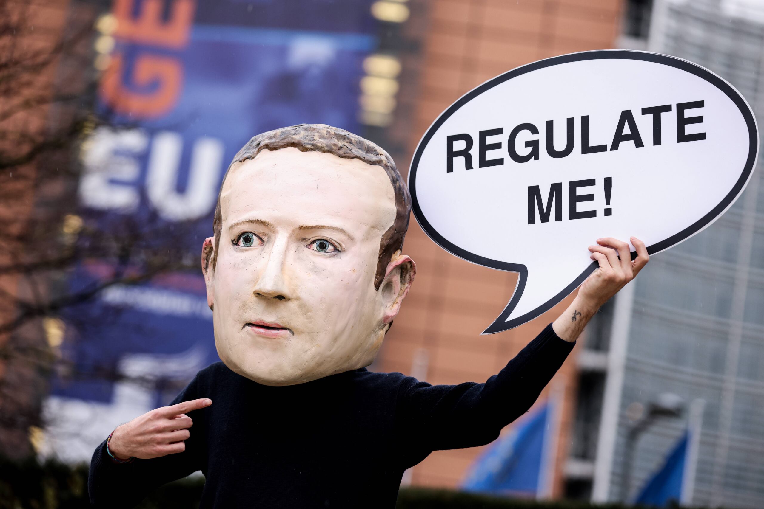Aktywista ekologicznej organizacji pozarządowej Avaaz w masce przedstawiającej prezesa Facebooka Marka Zuckerberga trzyma transparent z napisem "Regulate me" podczas akcji upamiętniającej wydanie ustawy o usługach cyfrowych, przed budynkiem Komisji Europejskiej w Brukseli 15 grudnia 2020 roku.